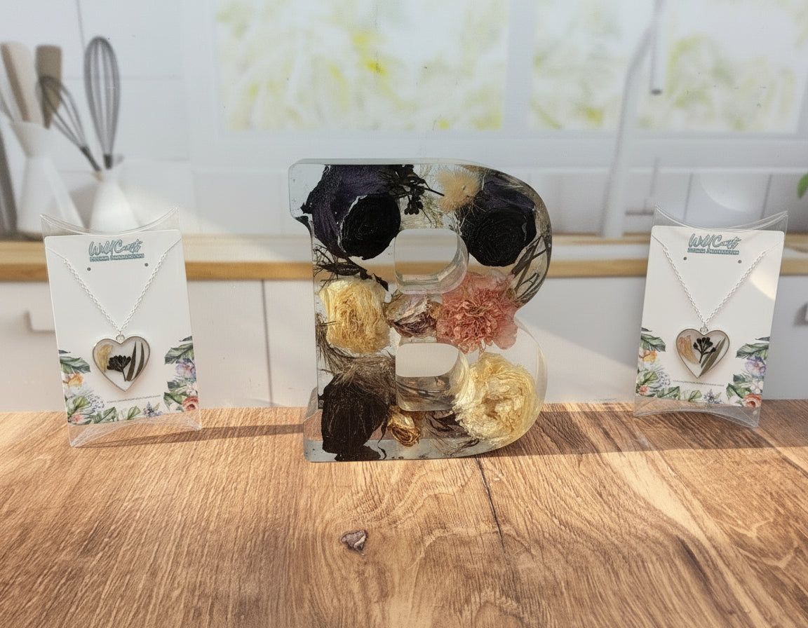 Decorative letter 'B' with flowers on a wooden surface, surrounded by necklaces in packaging.