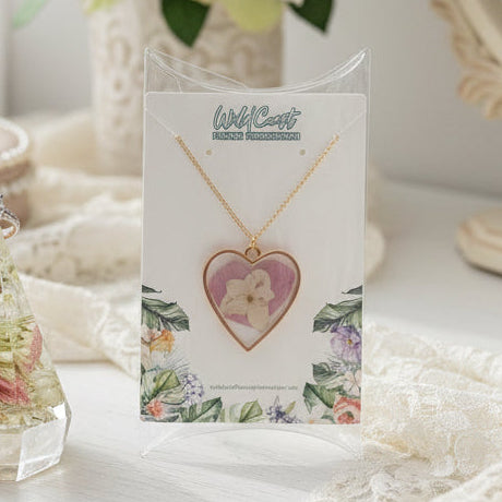Heart-shaped pendant necklace on a floral card with a decorative crystal on a wooden surface.