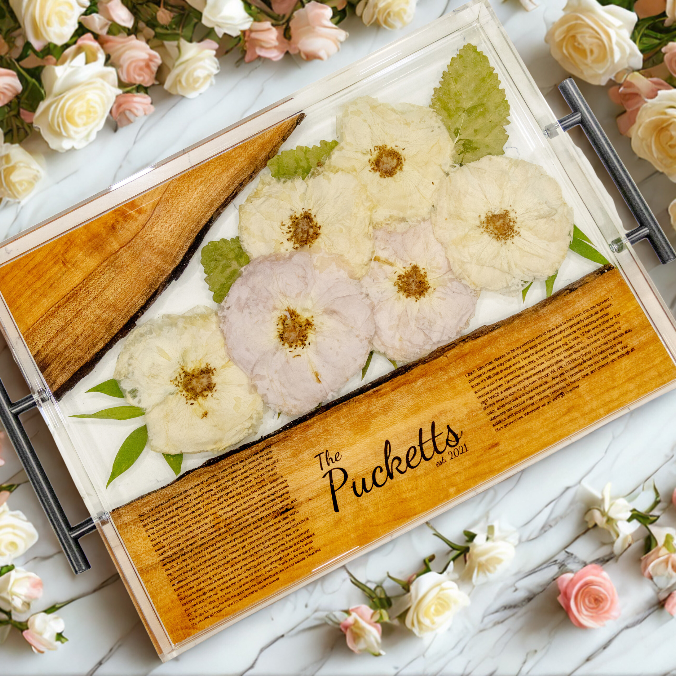 Wooden box with pressed flowers and 'The Pucketts' branding on a marble surface with flowers around.