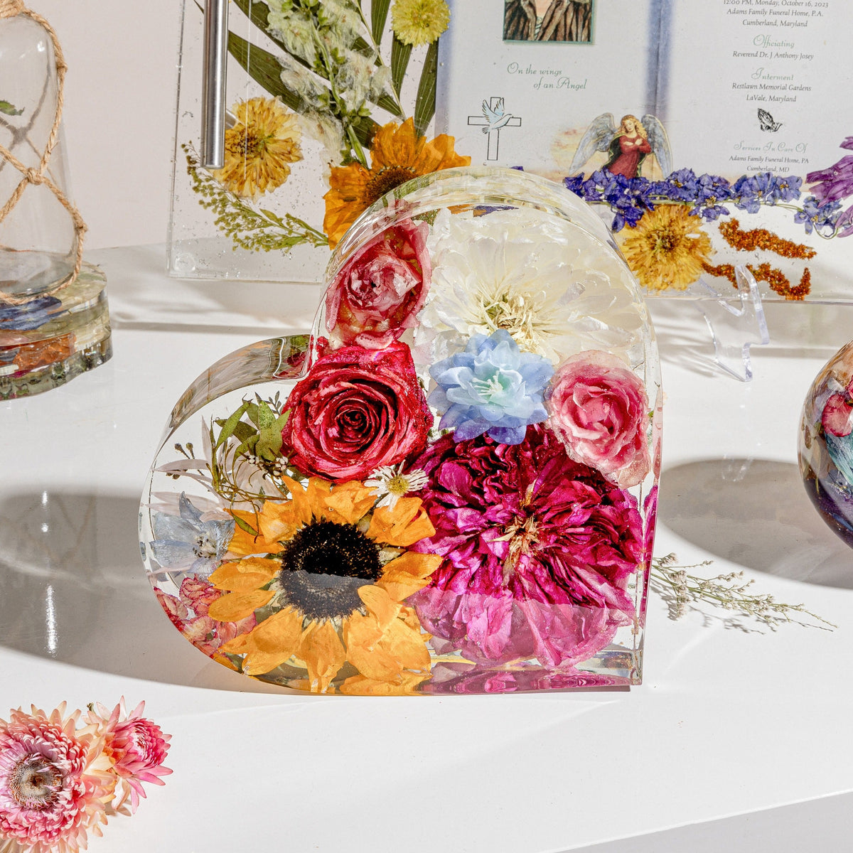 A heart-shaped resin bouquet block with preserved flowers, arranged inside with a clear resin finish, displayed on a flat surface.