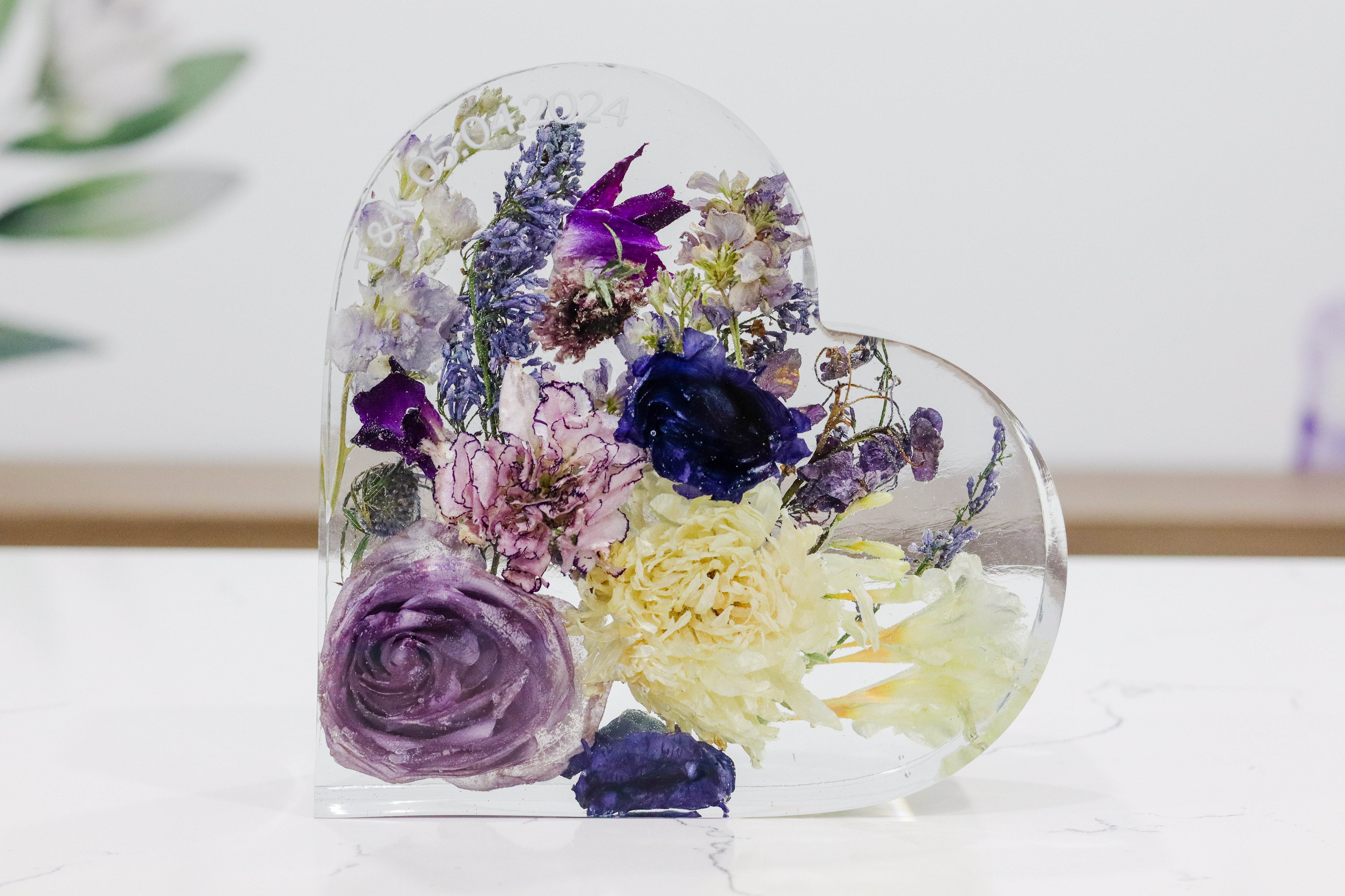 A heart-shaped resin bouquet block with preserved flowers, arranged inside with a clear resin finish, displayed on a flat surface.