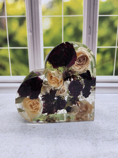 A heart-shaped resin bouquet block with preserved red and white roses arranged inside with a clear resin finish, displayed on a flat surface.
