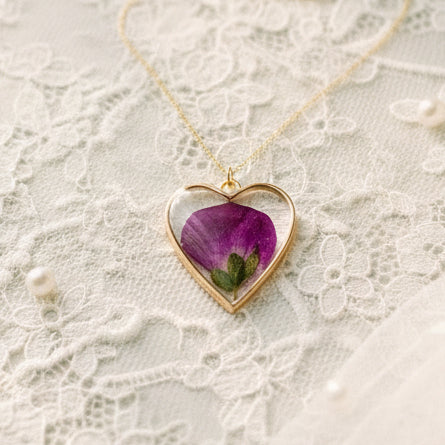 A heart-shaped pendant necklace with a purple dried flower preservation inside, displayed on lace cloth