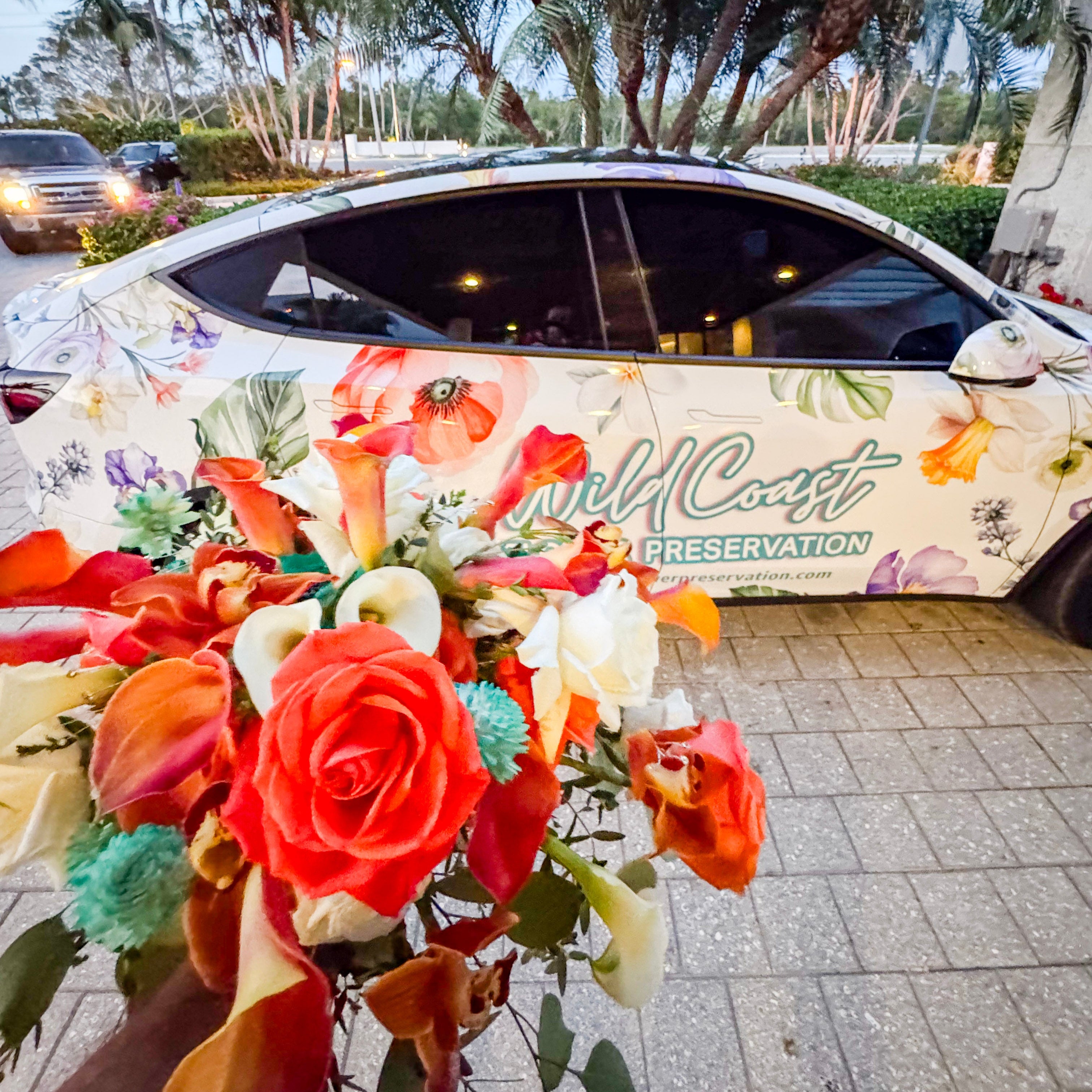 Wild Coast Flower Car with floral design and 'Wild Coast' text by a scenic waterfront with a fresh bouquet picked up from a nearby wedding.