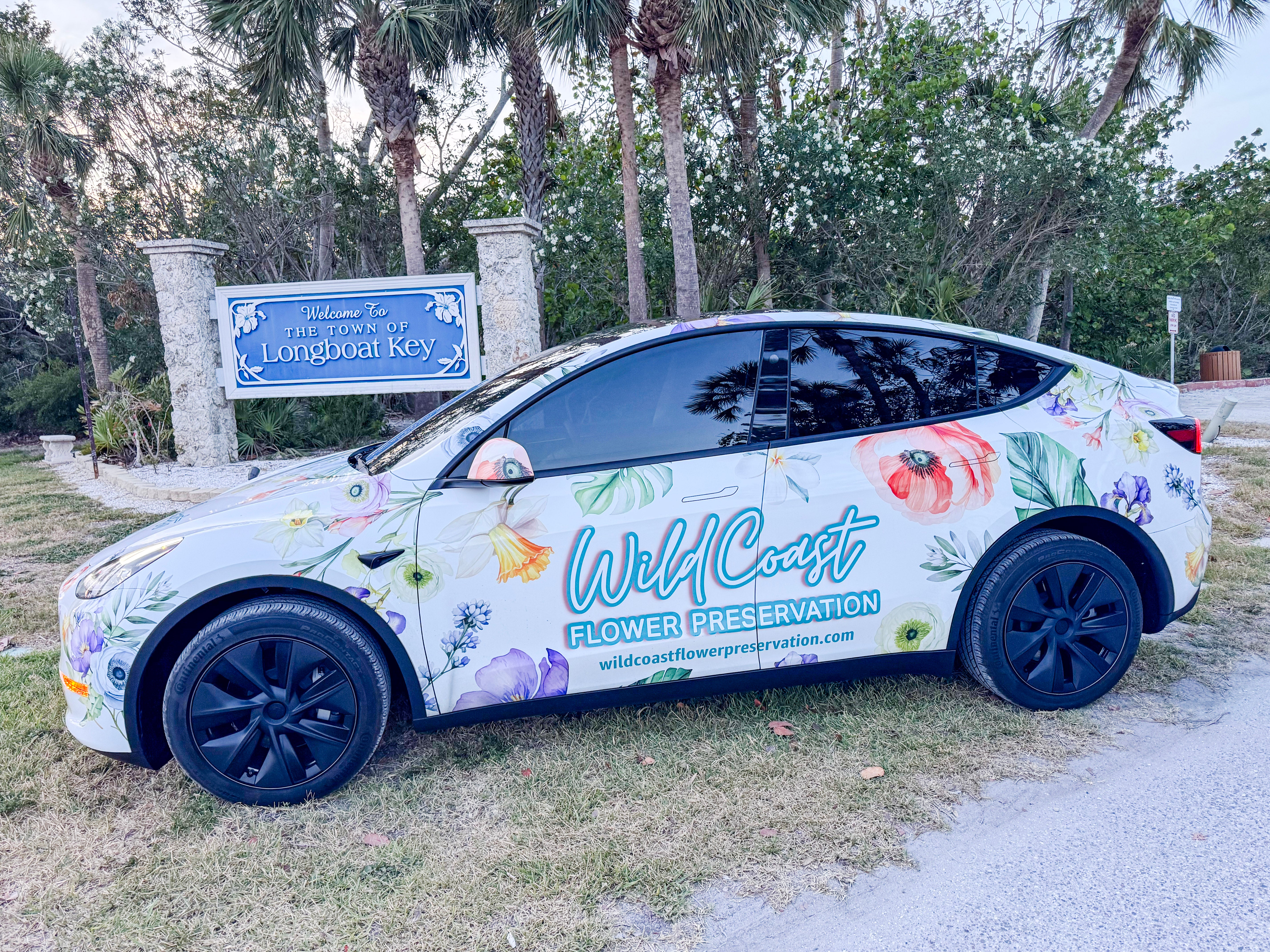 Car with floral design and 'Wild Coast Flower Preservation' branding parked in front of West Coast of Florida Wedding Venue, Longboat Key Bouquet Preservation Pickup Service