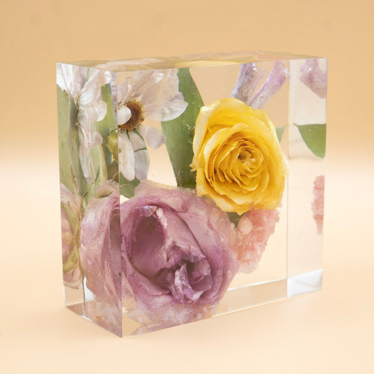 Clear resin bouquet preservation in 5-inch cube featuring daisy and roses on a beige surface