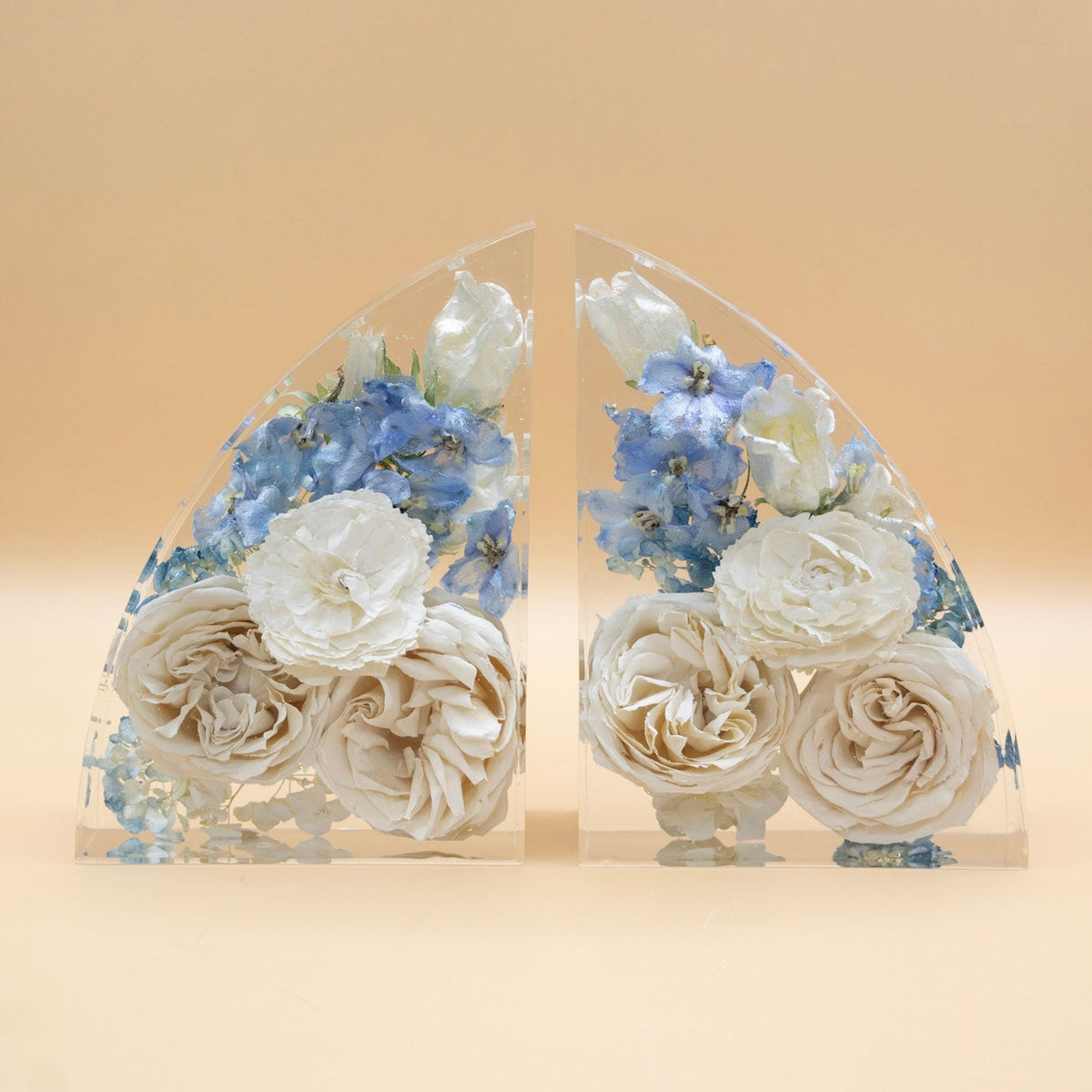 Blue delphinium, white ranunculus and white rose with color correction service suspended in clear epoxy resin bouquet preservation bookends about 7-inches tall on a beige background
