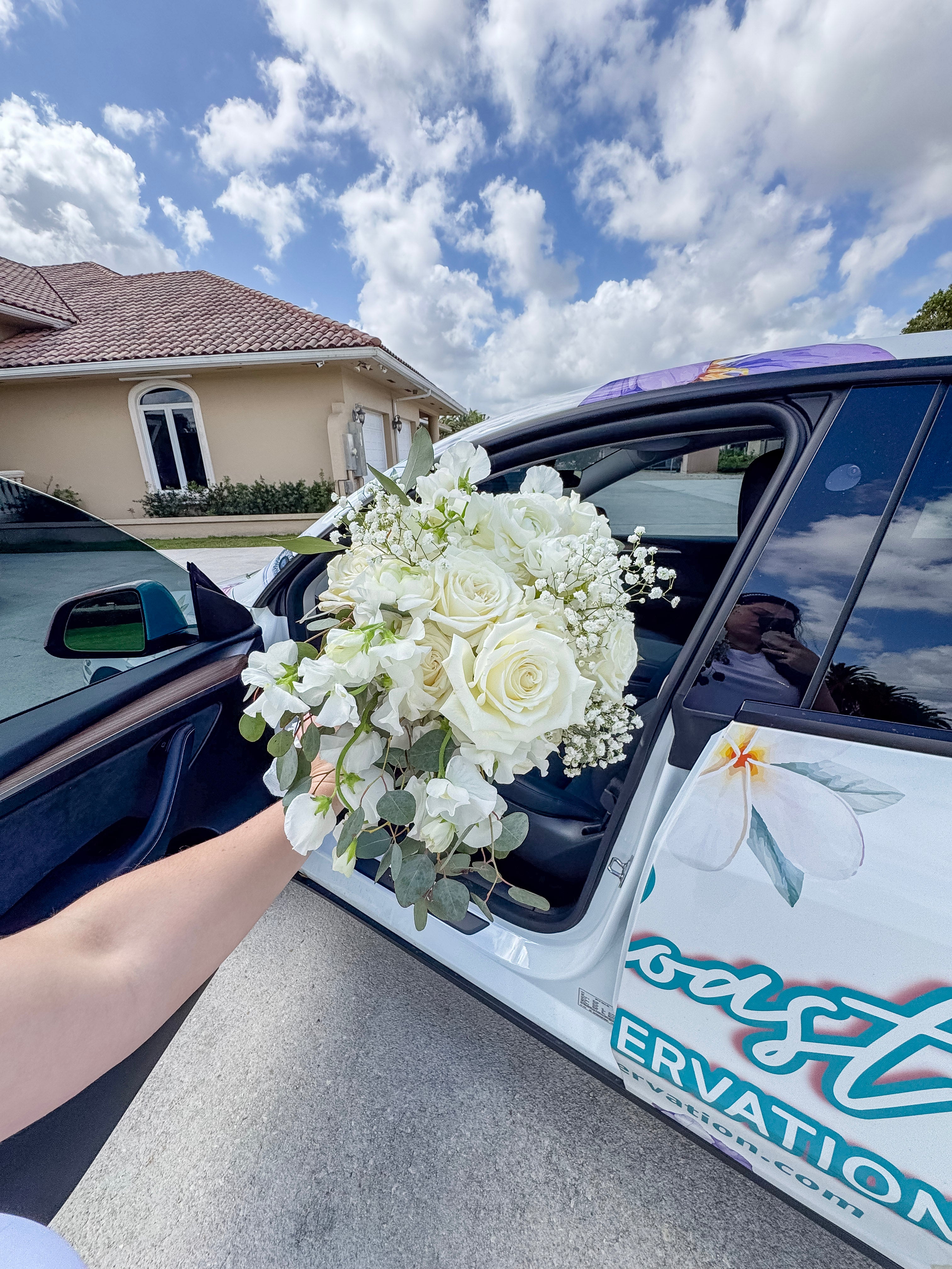 Wild Coast Flower Car with floral design and 'Wild Coast' text by a scenic waterfront with a fresh bouquet picked up from a nearby wedding.