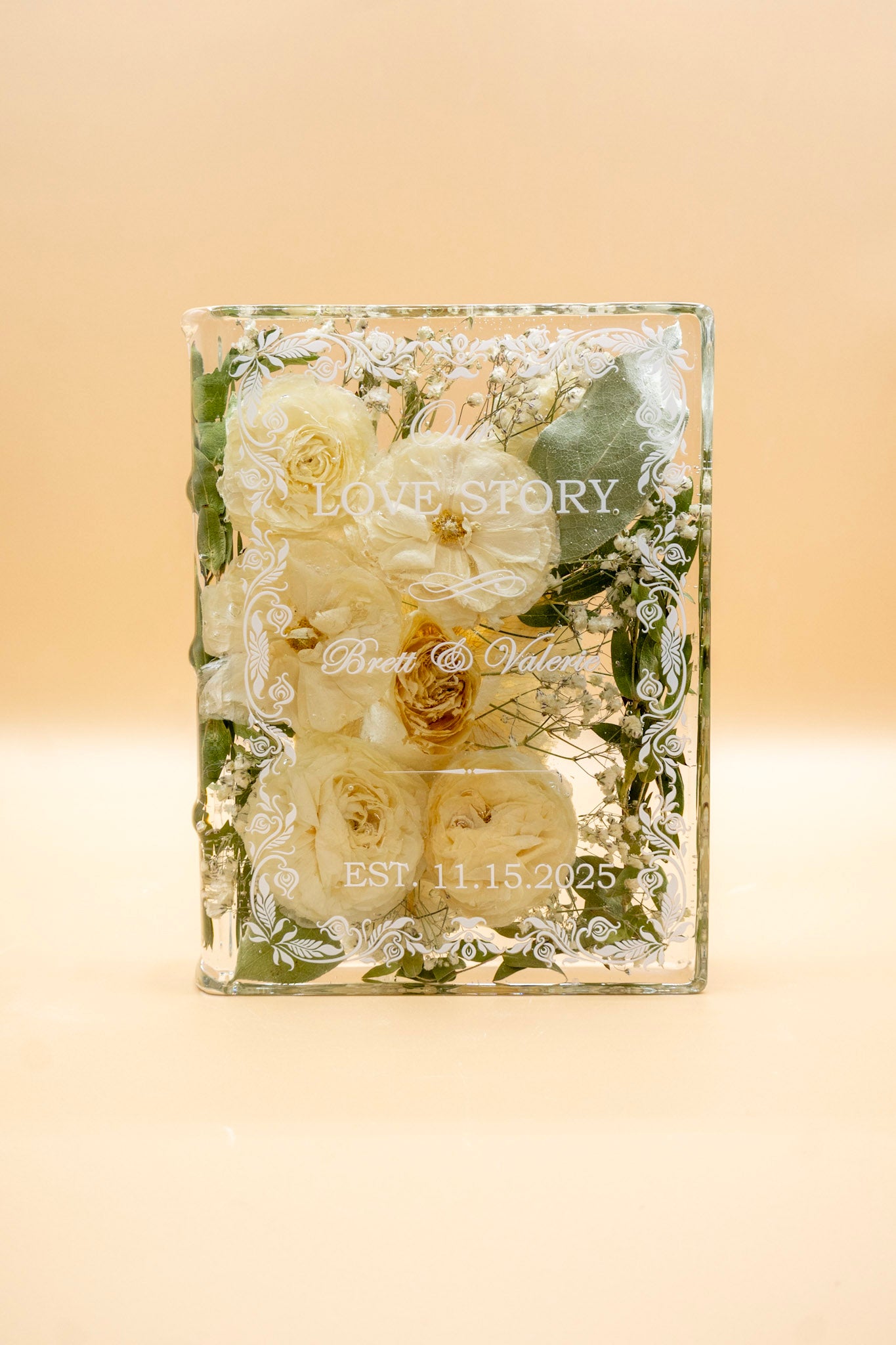 Book-shaped resin keepsake preserving white wedding roses, baby's breath and eucalyptus with the couple's names and date engraved.