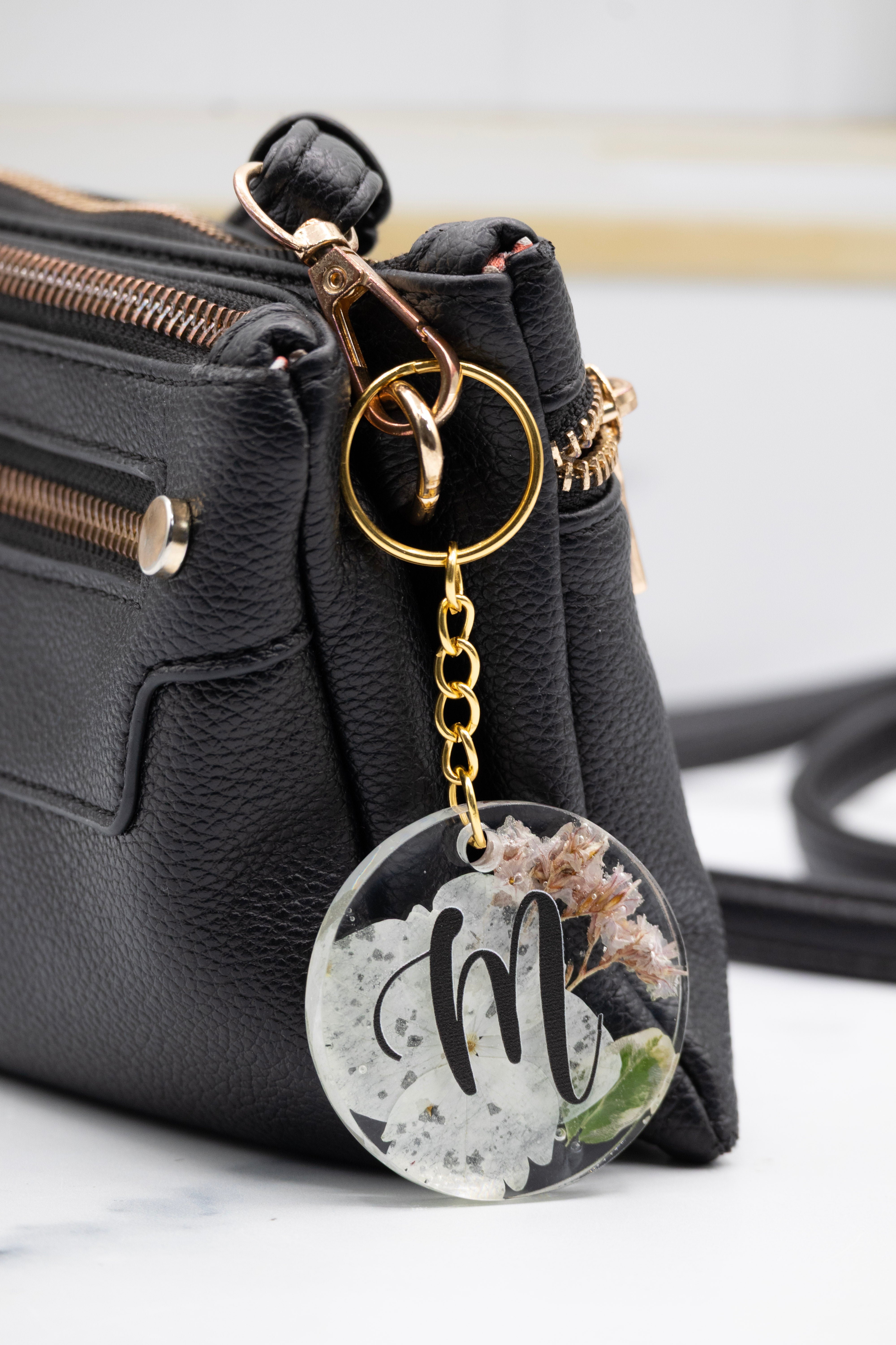 Black handbag with a keychain featuring a floral design and letter 'm' on a white background