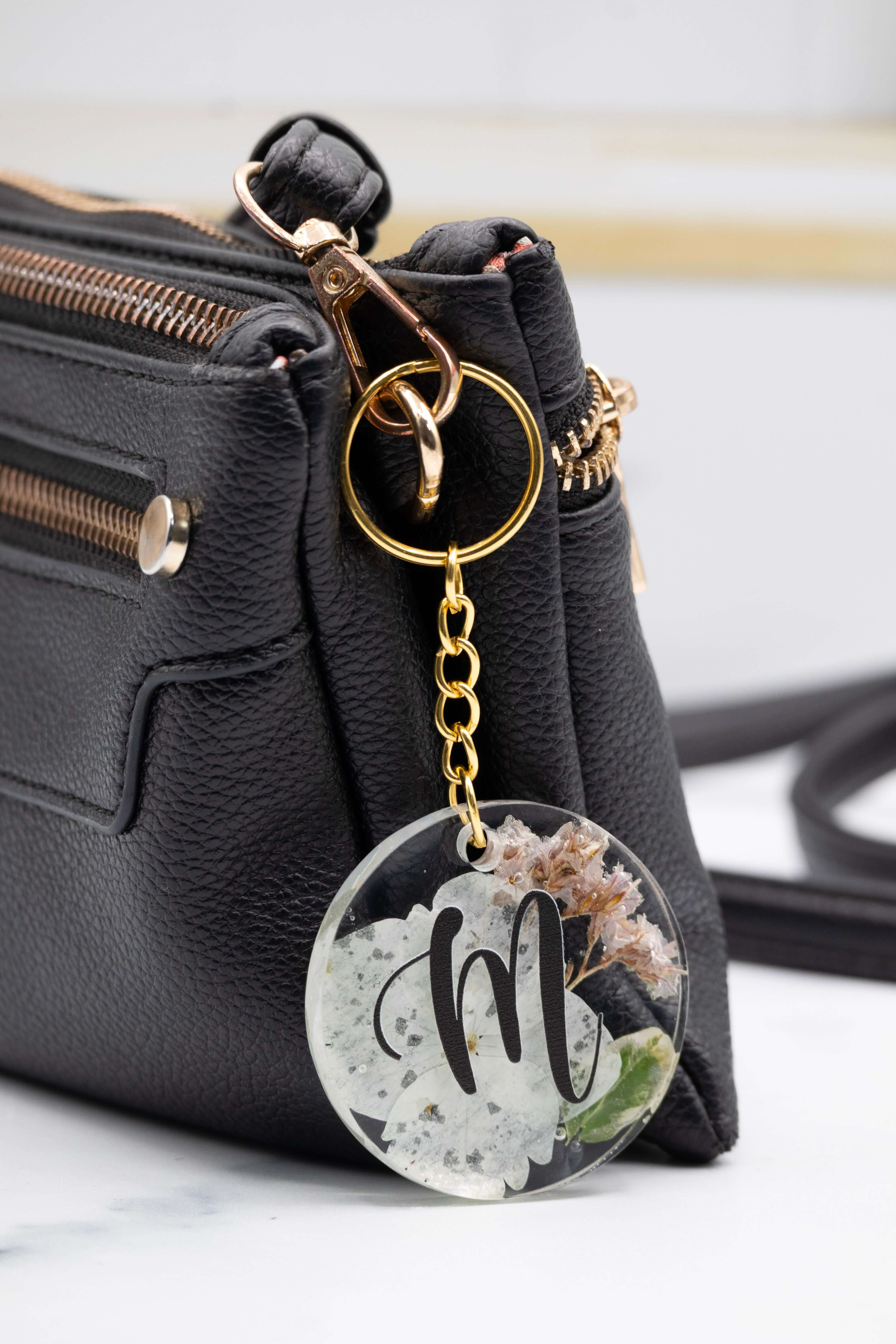 Black handbag with a keychain featuring a floral design and letter 'm' on a white background