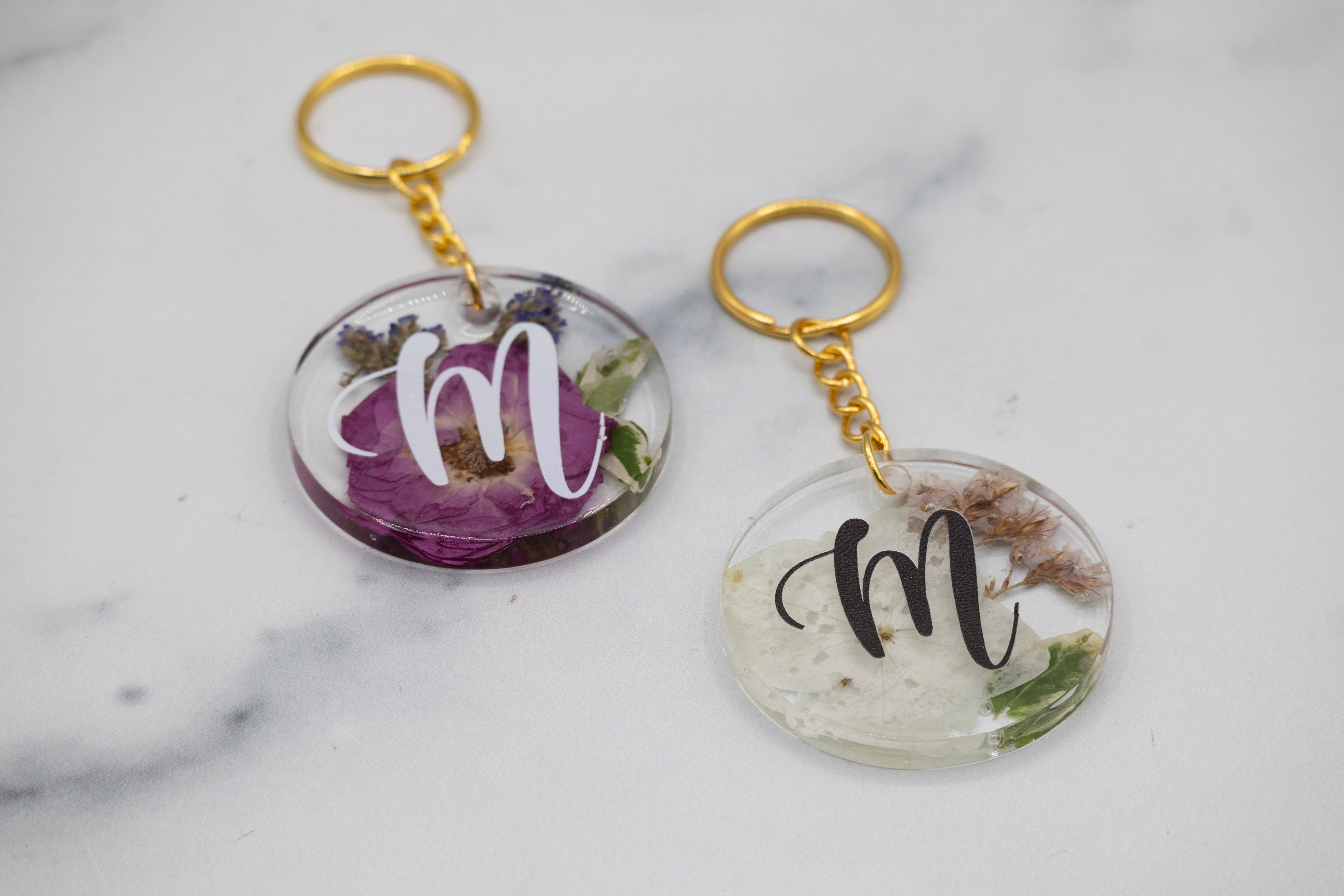 Two keychains with floral designs and monograms on a marble surface. Wedding Bouquet Preservation Keychain Round Pressed Flower Keychain Flower Preservation Custom Keychain Preserved Bouquet Keychain