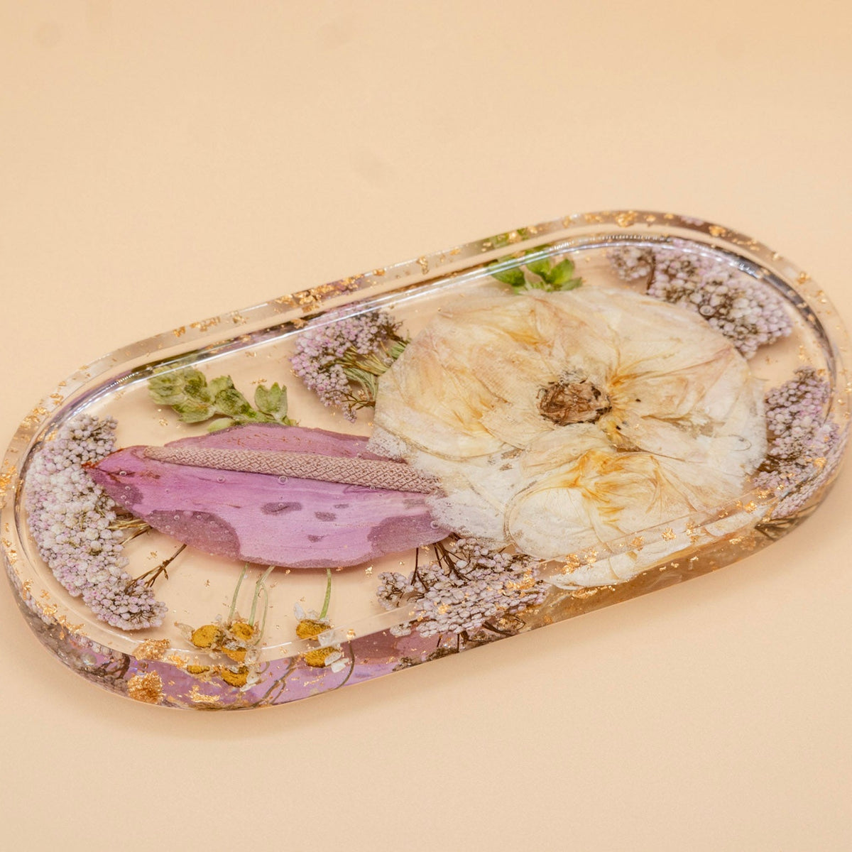 An oval resin tray featuring pressed garden rose and pink anthurium, displayed on a solid beige background.
