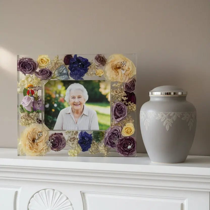 Memorial photo frame with flowers and an urn on a white surface.
