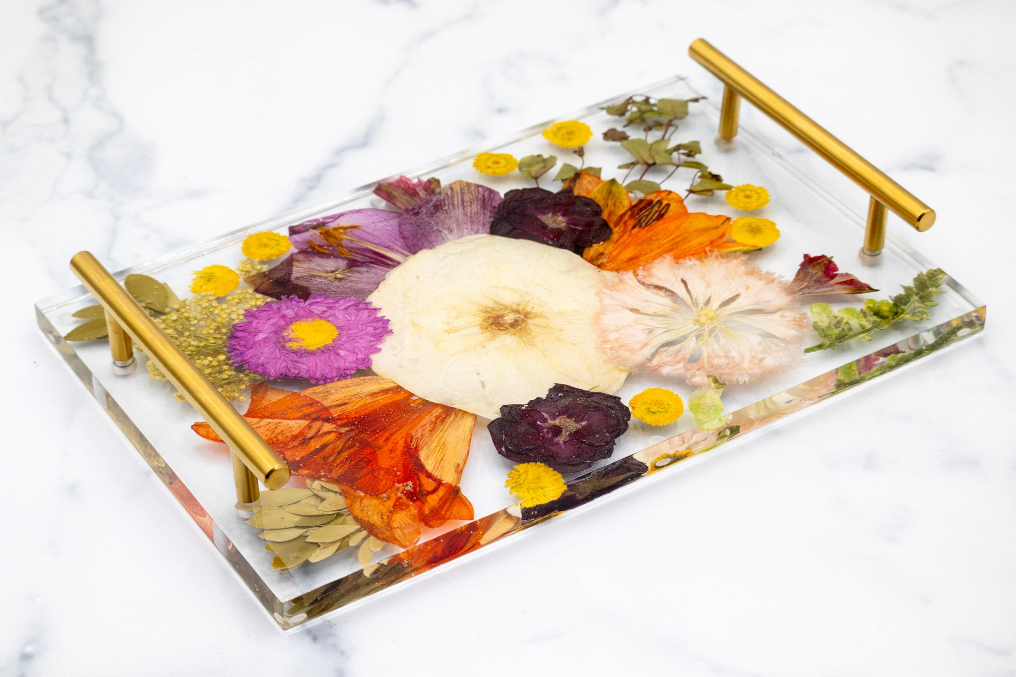Decorative tray with pressed flowers and gold handles on a marble surface