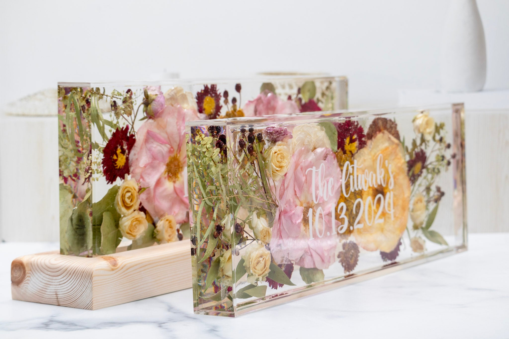 Decorative acrylic block with pressed flowers and personalized text on a white surface.