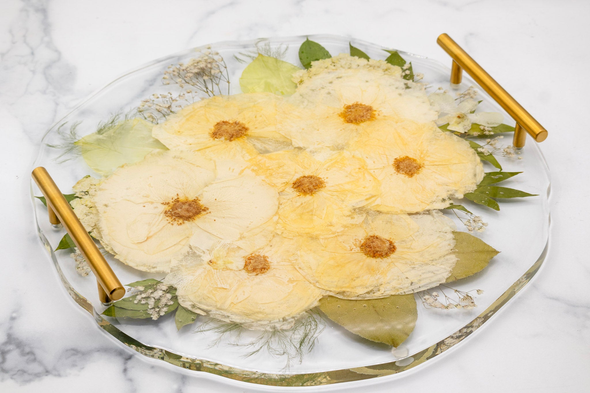 Pressed White rose preservation in epoxy resin round serving platter with gold handles on a marble surface
