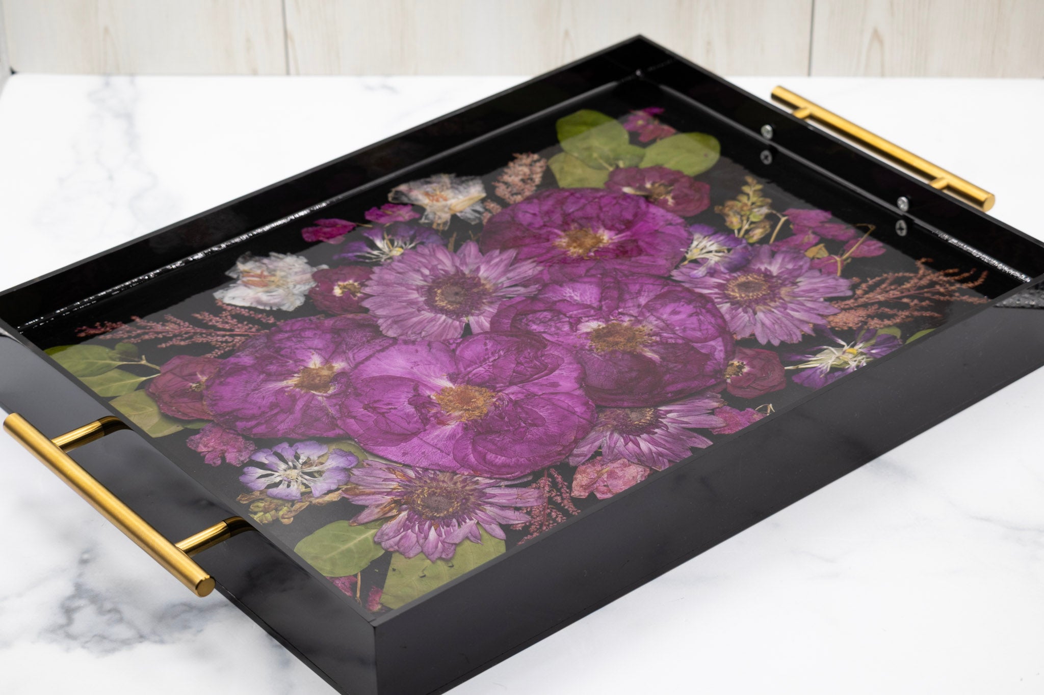 Black tray with floral design and gold handles on a white marble surface