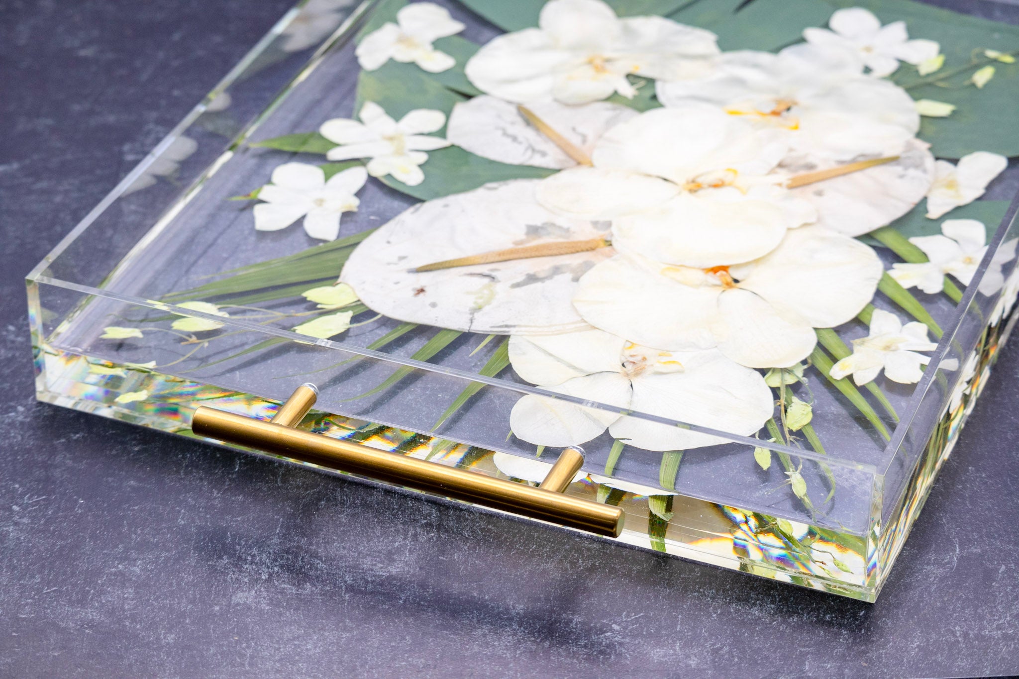Preserved white tropical bouquet preservation in pressed flower serving tray with raised edges and gold handles on a black background