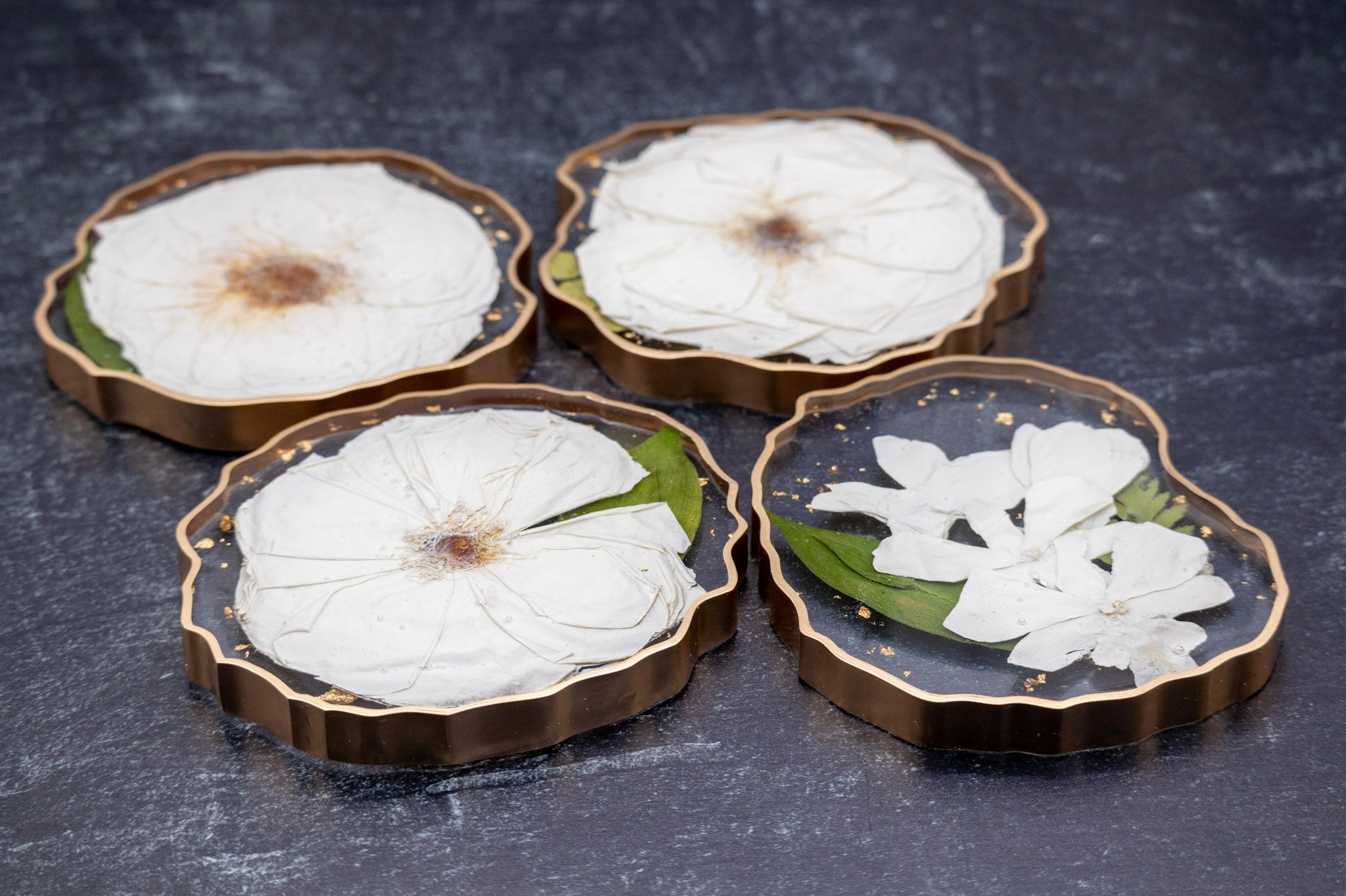 Four decorative coasters with pressed flowers on a dark surface