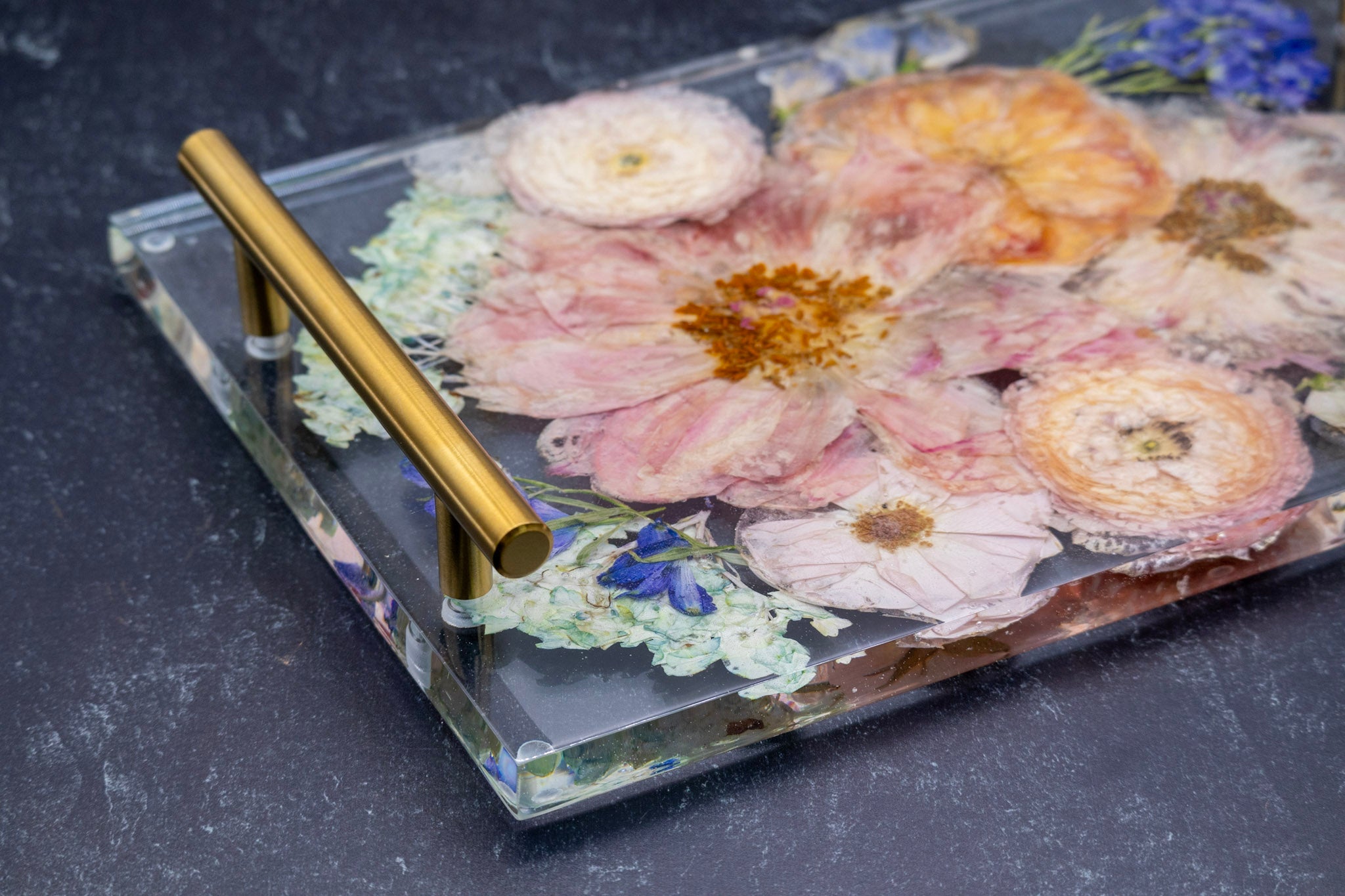 Epoxy Resin Flower Preservation tray with pressed flowers and gold handle on a dark surface