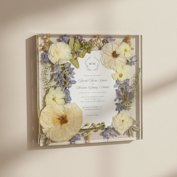 clear Resin wall art with encased wedding invitation and pressed flowers on a beige wall