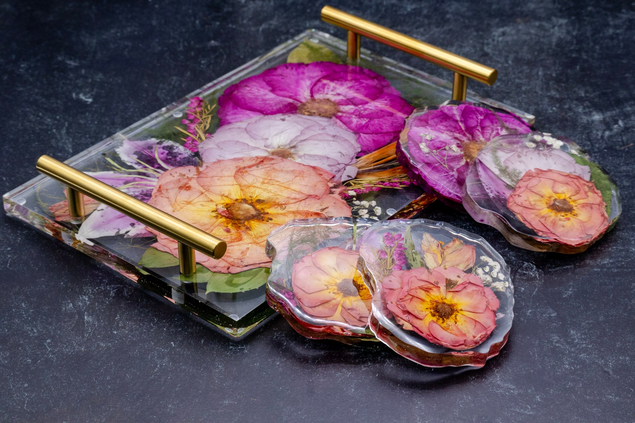 Set of pressed flower coasters with resin serving tray with gold handles on a dark surface