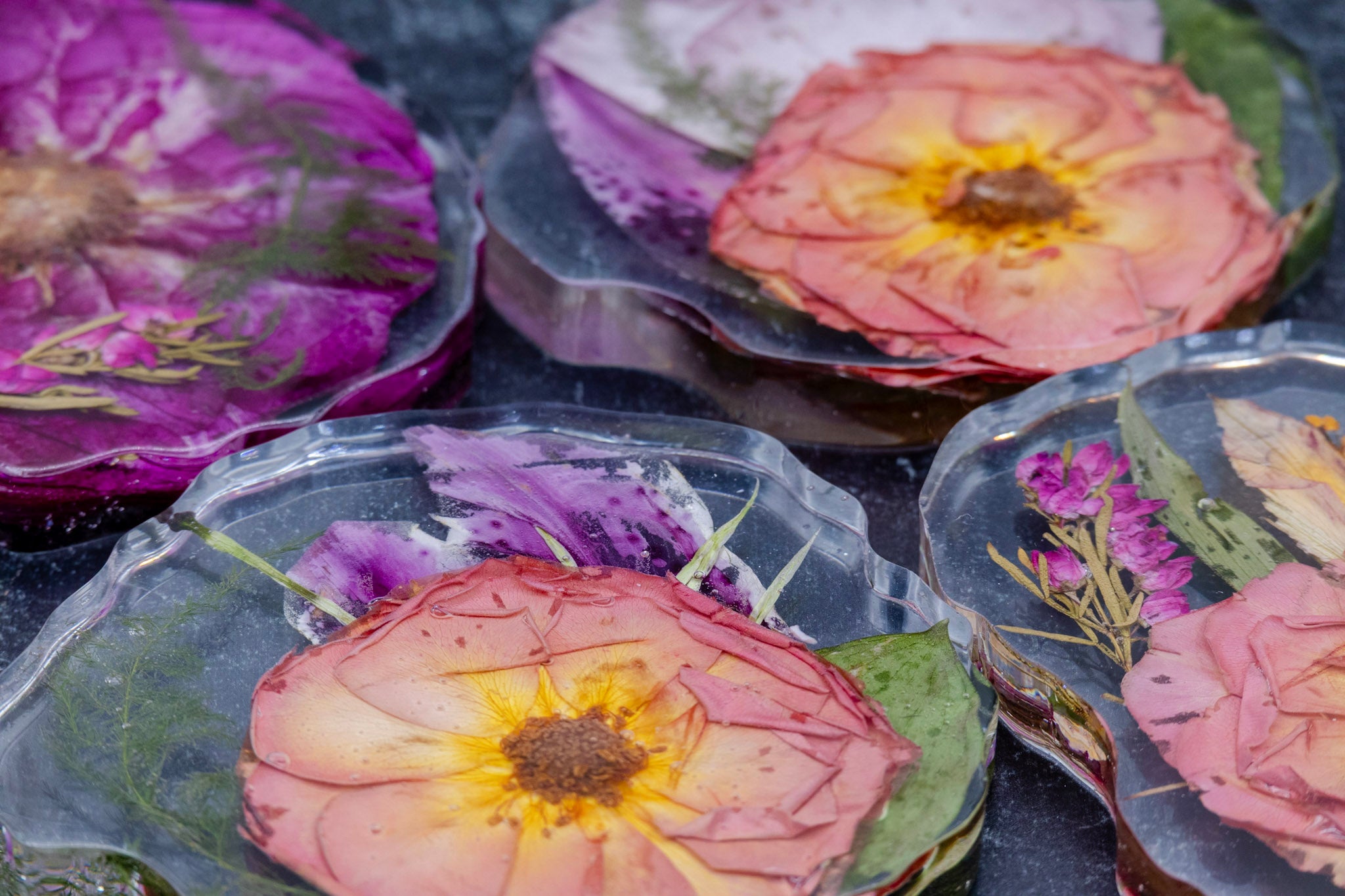 Pressed flower resin coasters with colorful floral designs on a dark surface