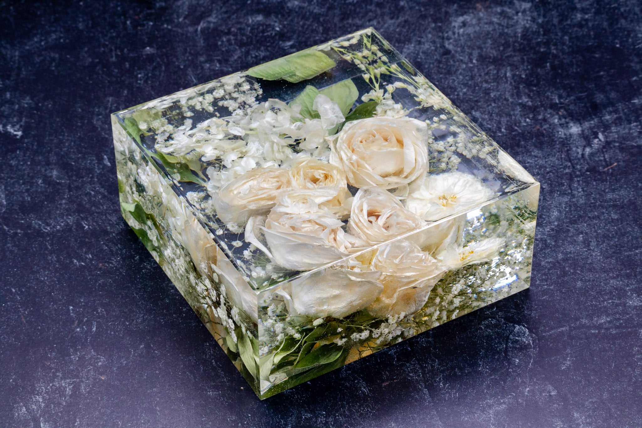 Clear resin block with embedded white roses on a dark background