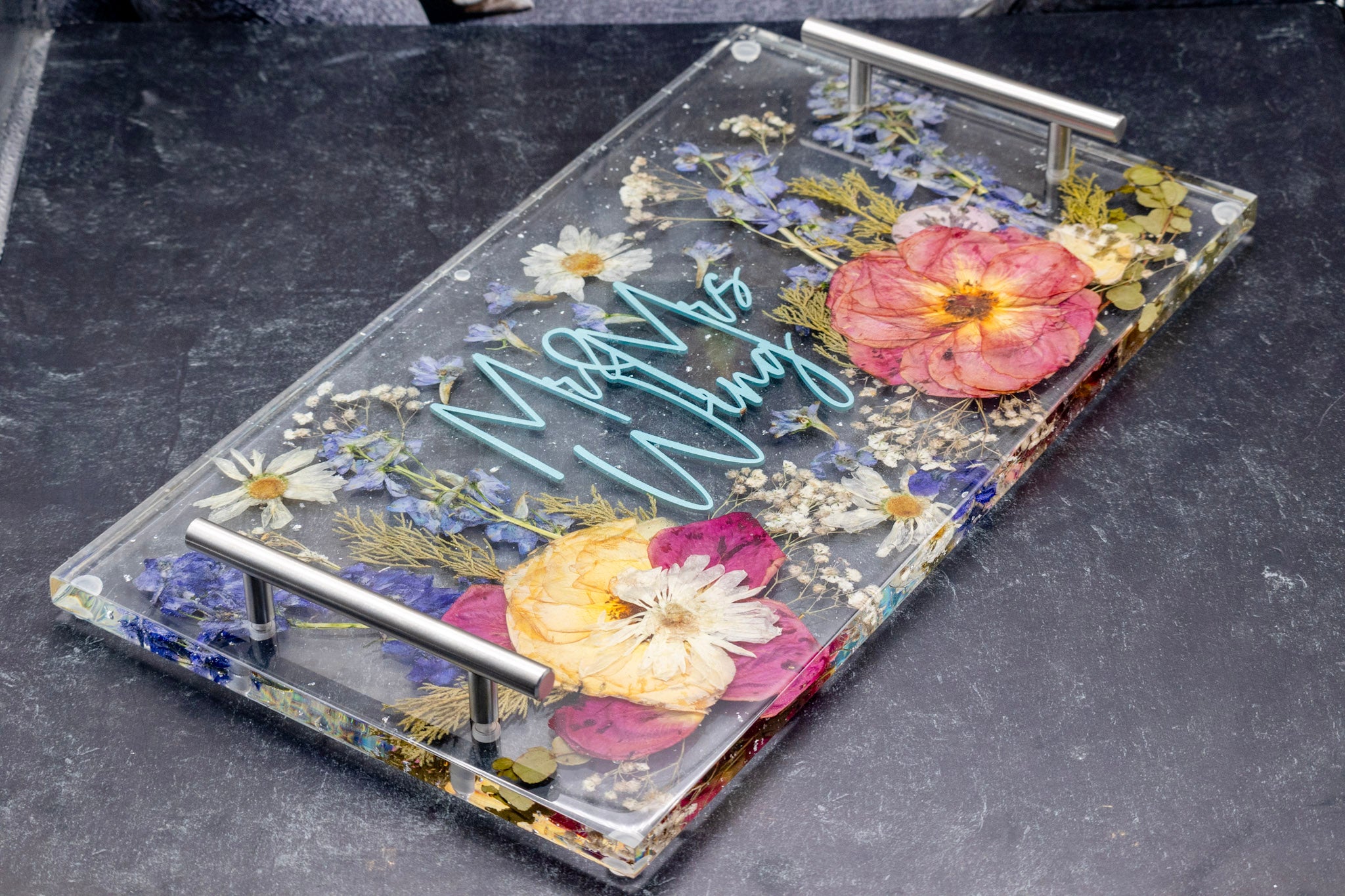 Resin tray bouquet preservation epoxy serving tray with pressed flowers encased with cake topper. Epoxy flower preservation tray with silver handles.