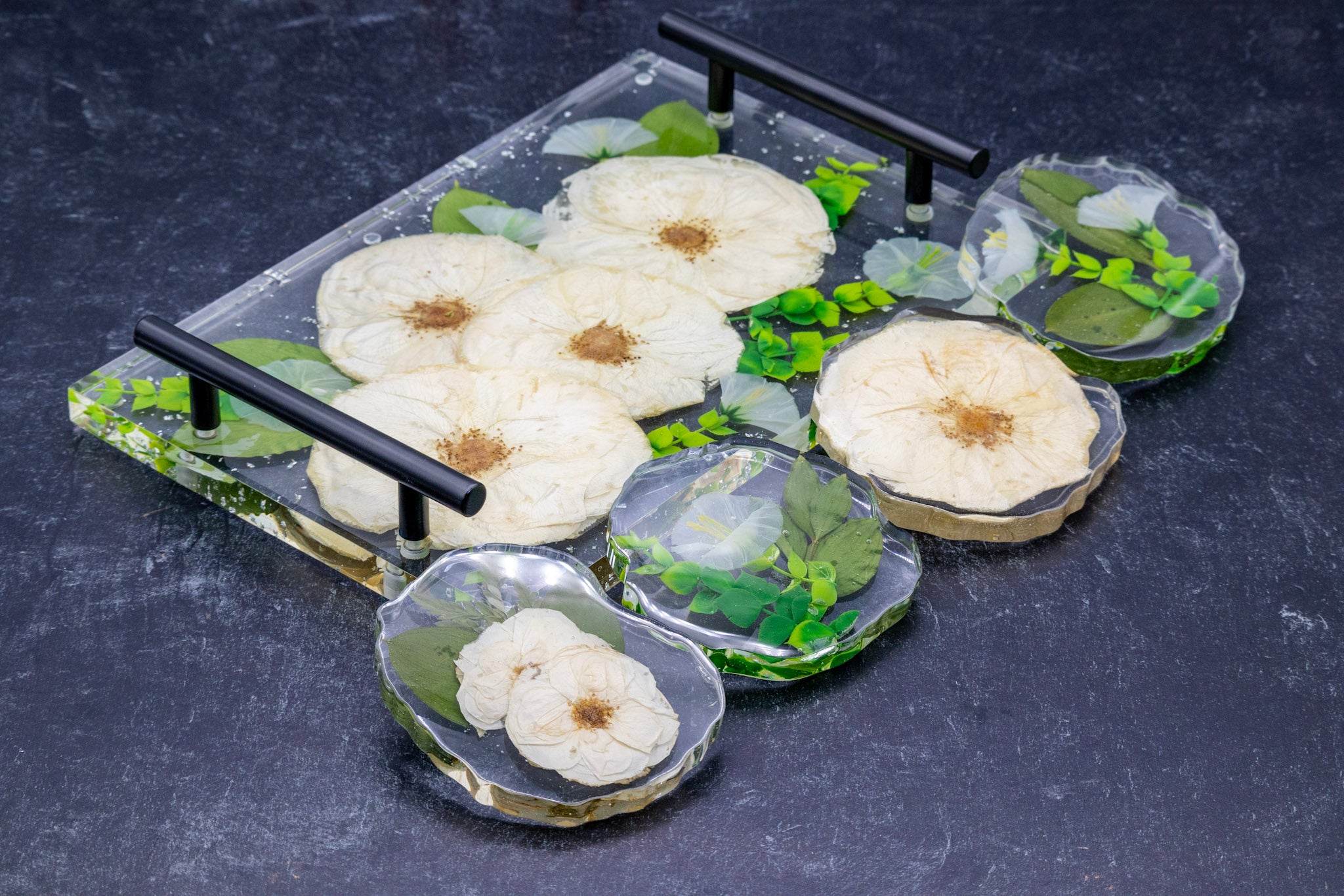 Decorative resin tray with white pressed flowers and green leaves on a dark surface