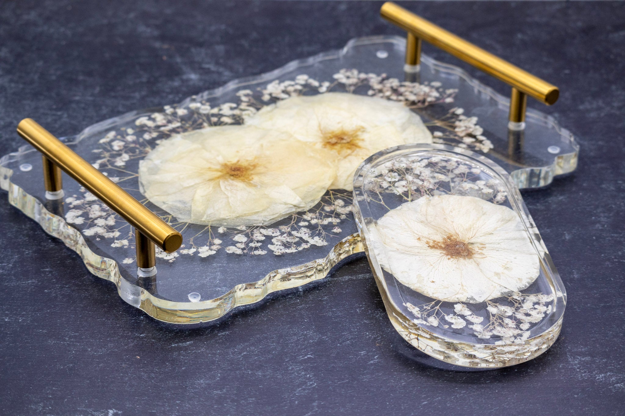 Clear glass tray with gold handles featuring pressed white flowers on a dark surface dried rose and baby breath preserved flower tray