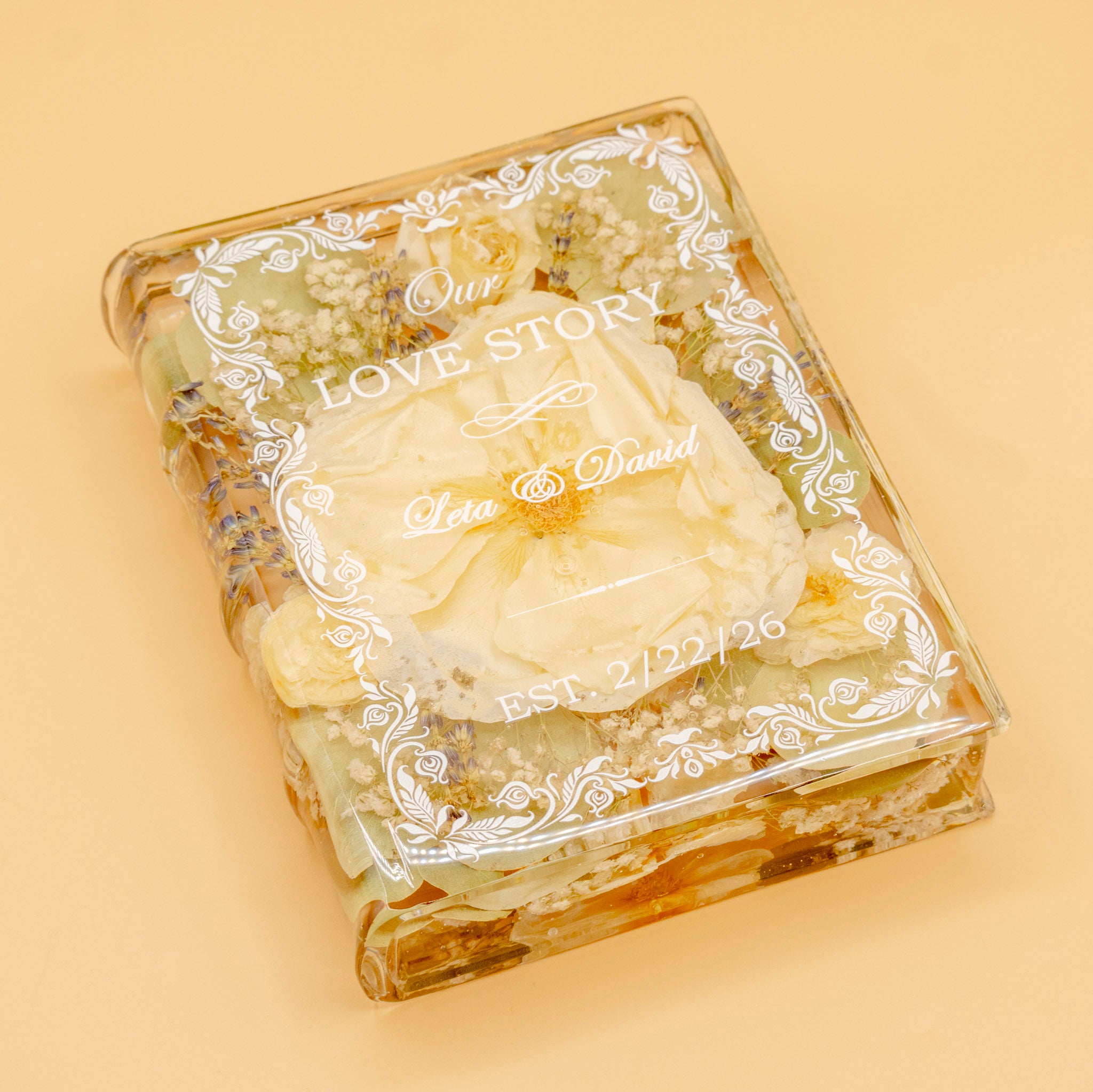 Book-shaped resin keepsake preserving an ivory wedding rose, lavender and baby's breath, engraved with a couple's names and date.