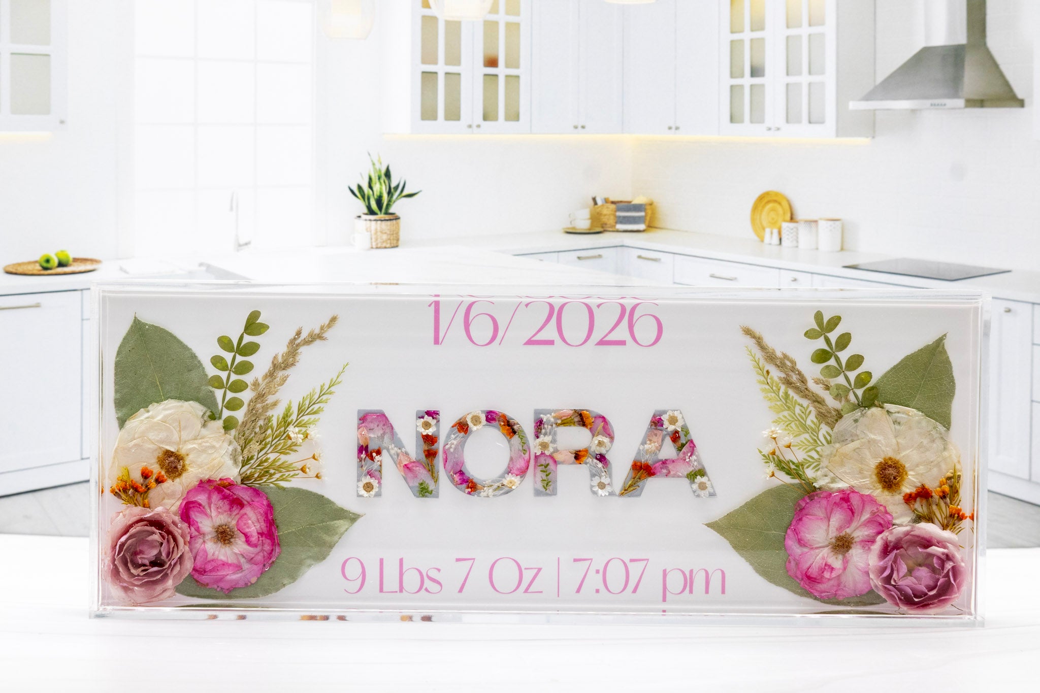 Decorative baby announcement sign with floral designs and text in a kitchen setting