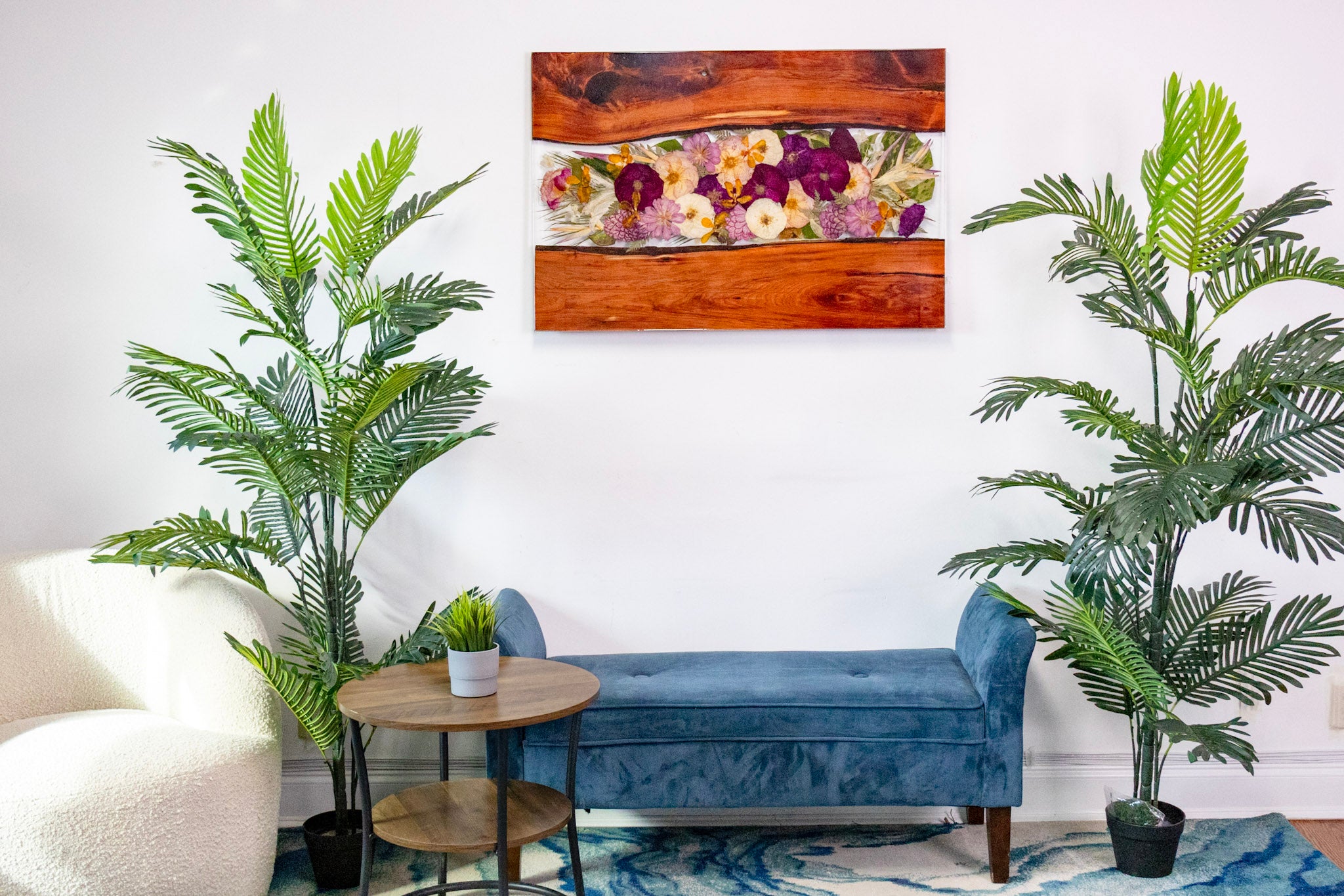 Large resin wall decor 40x27 live edge wood and pressed flower wall art hanging on the wall of a Living room with a blue bench, white sofa, and decorative plants.
