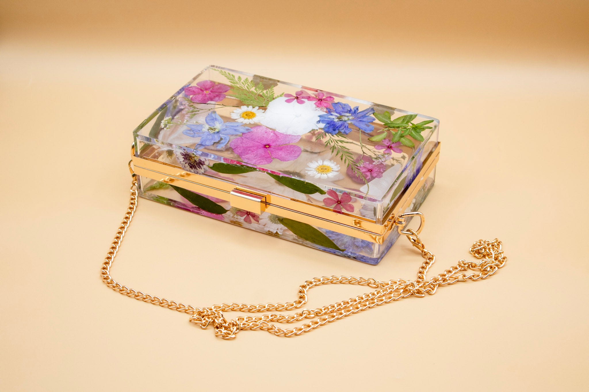 Resin Flower clutch bag with a gold chain on a beige background