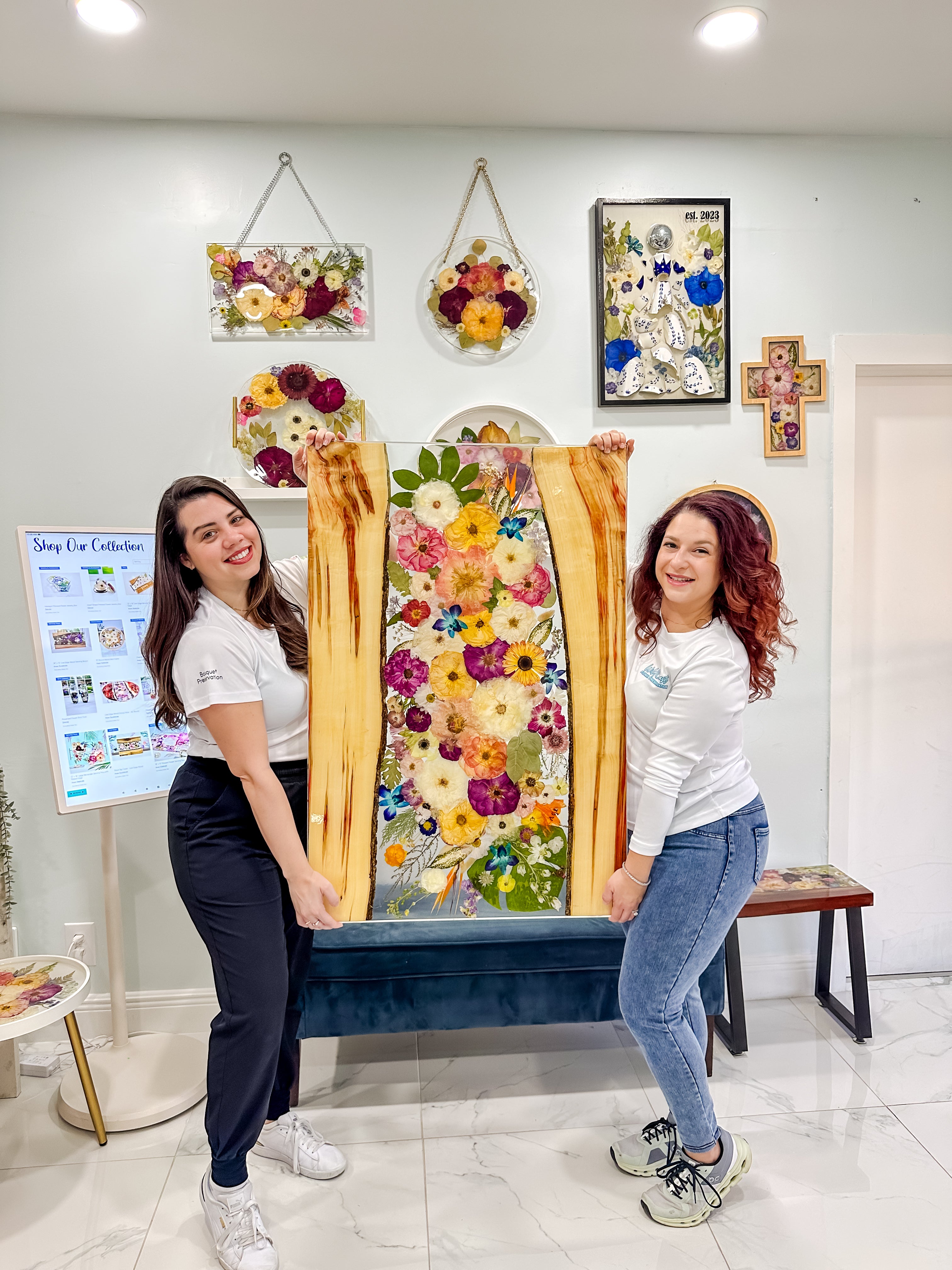 Two women holding a large floral arrangement in a room with decorative wall art.
