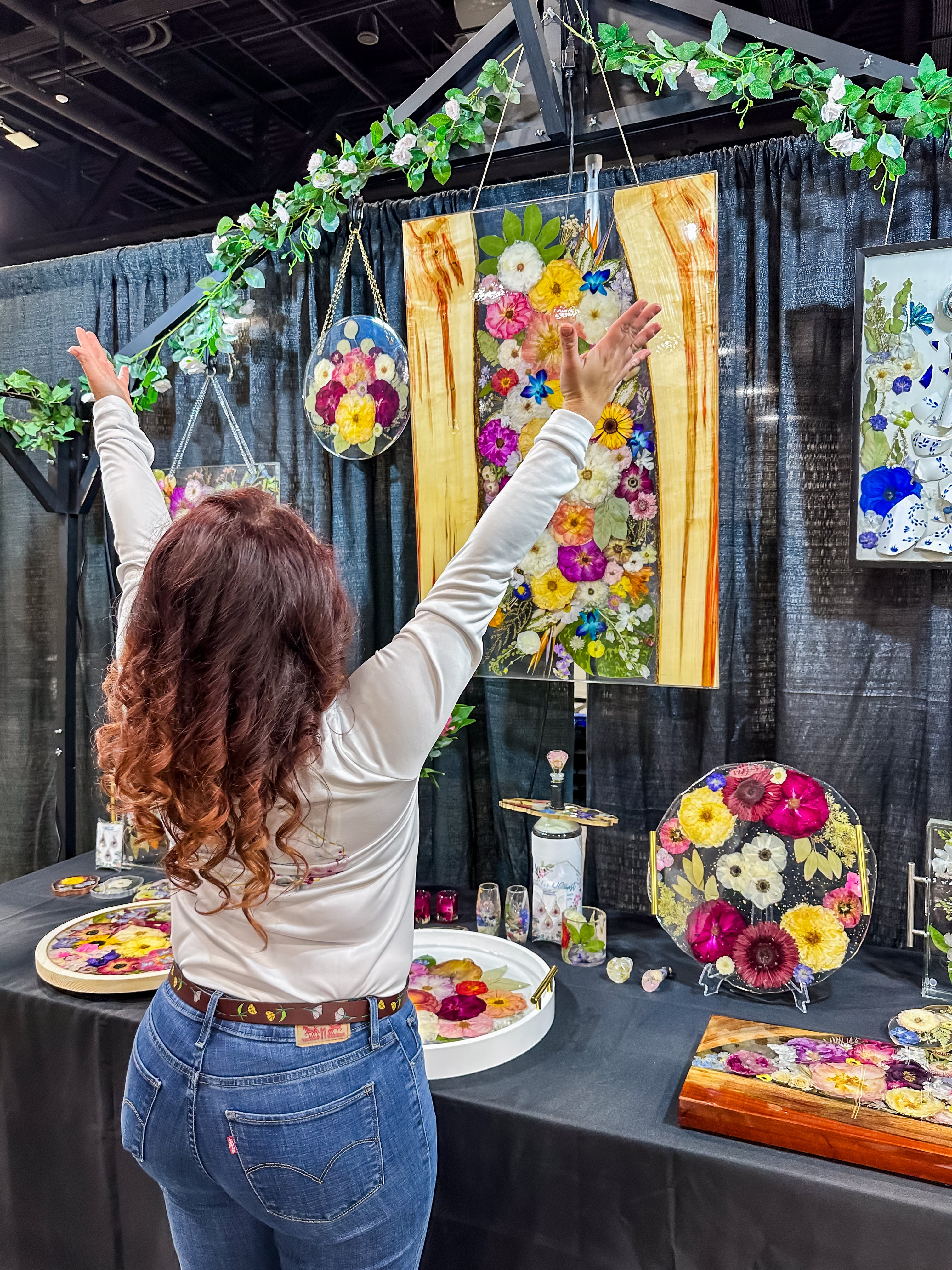 Woman standing in front of a table with floral art pieces at an event.