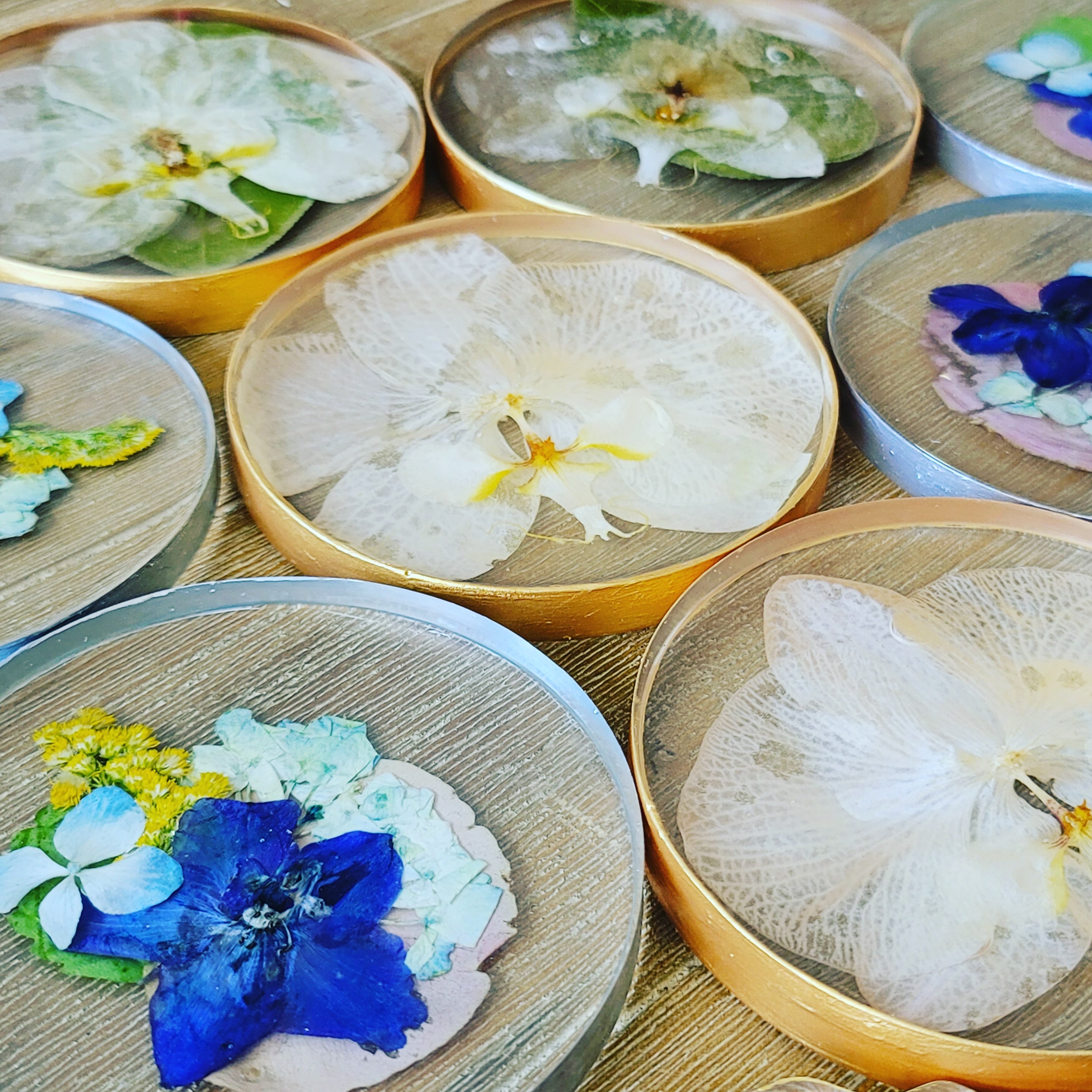 Two round resin coasters with pressed flowers, one with a gold edge and the other with a silver edge, displayed on a white background.