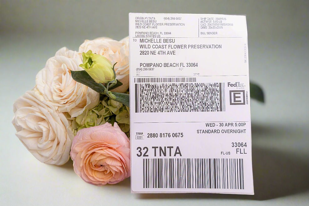 A printed FedEx Priority Overnight shipping label with a barcode and tracking information, displayed in front of a arrangement of pink roses.