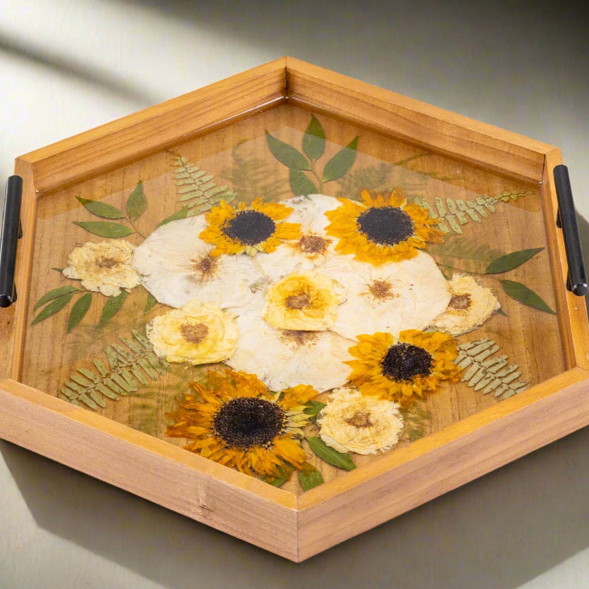 Wide landscape photo of a wood hexagon ottoman tray with pressed flowers encased in clear epoxy resin in a bright window setting