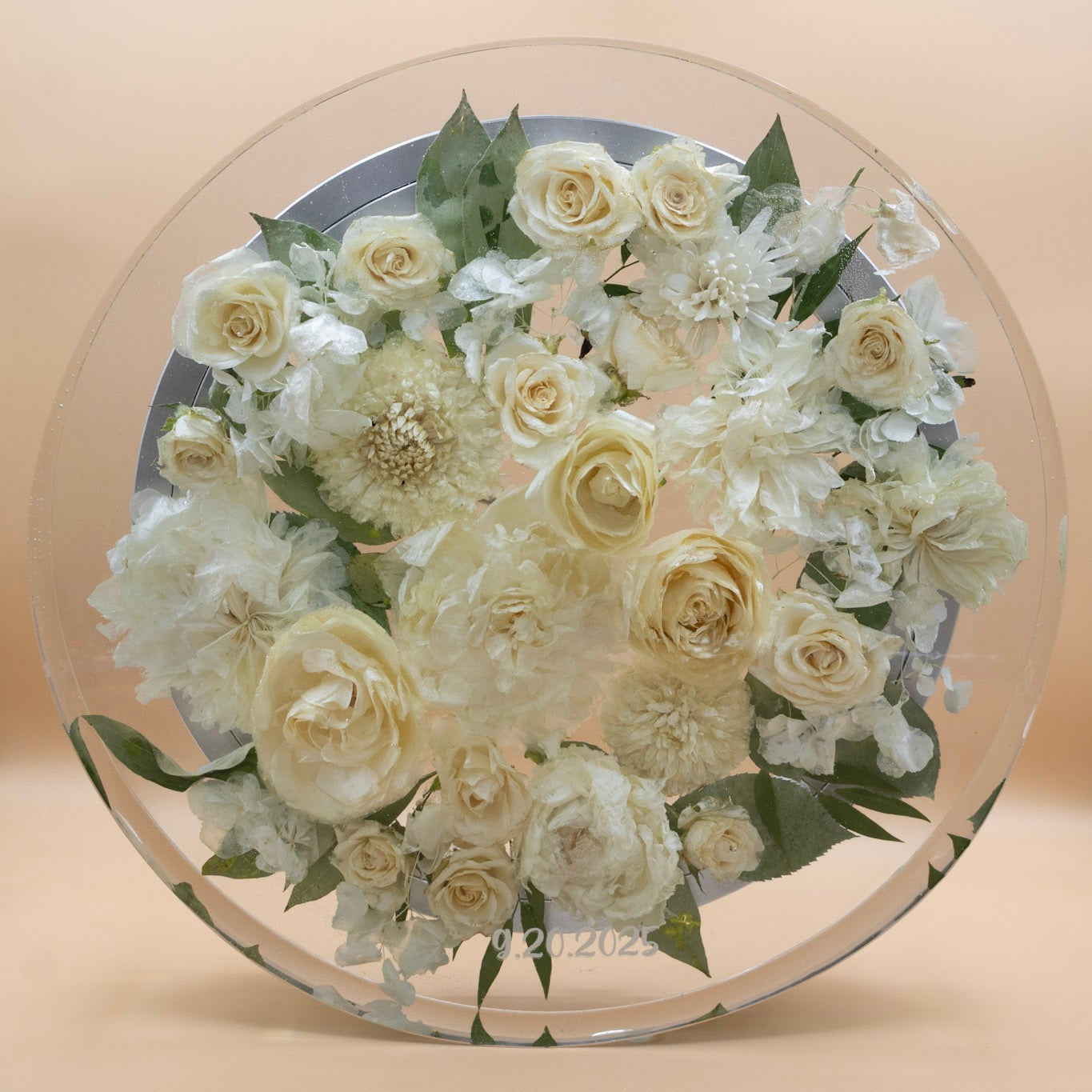 Standing view of A preserved flower lazy susan whole white peony and white dahlia dried flowers and green leaves, encased in resin lazy susan with rotating base set against a solid beige background.