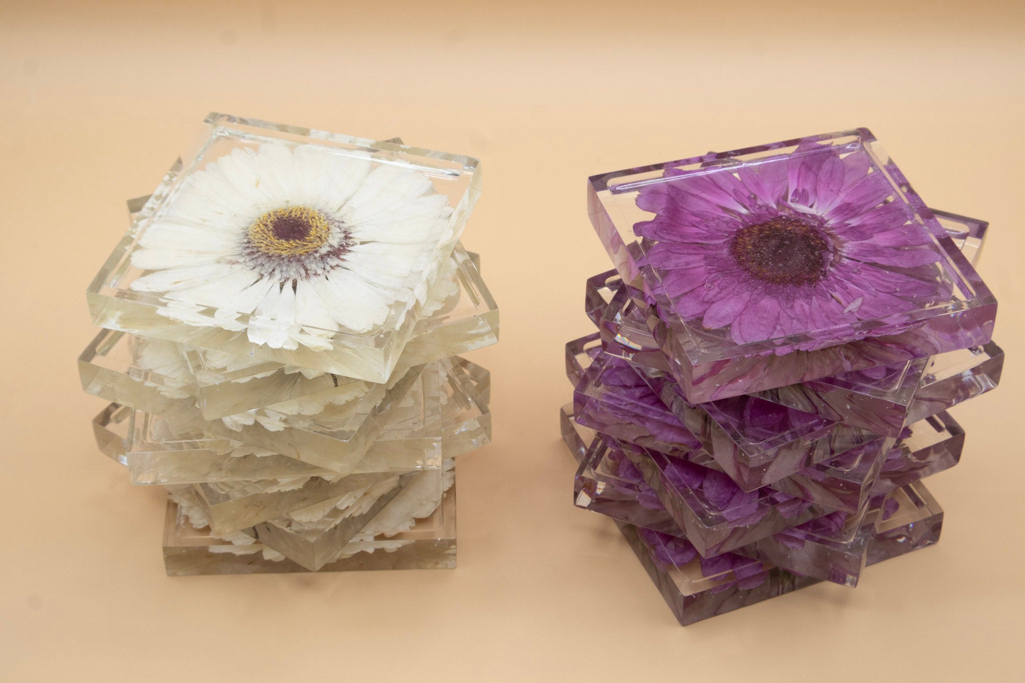 Stacks of square coasters with pressed flowers on a beige background