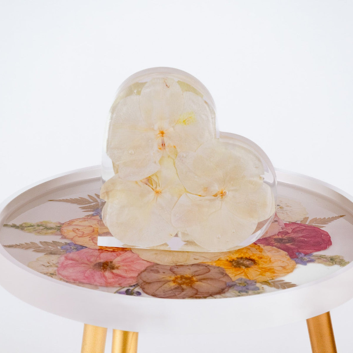 White orchid bouquet preservation inside of resin heart mold on a white table with preserved resin flowers on top.