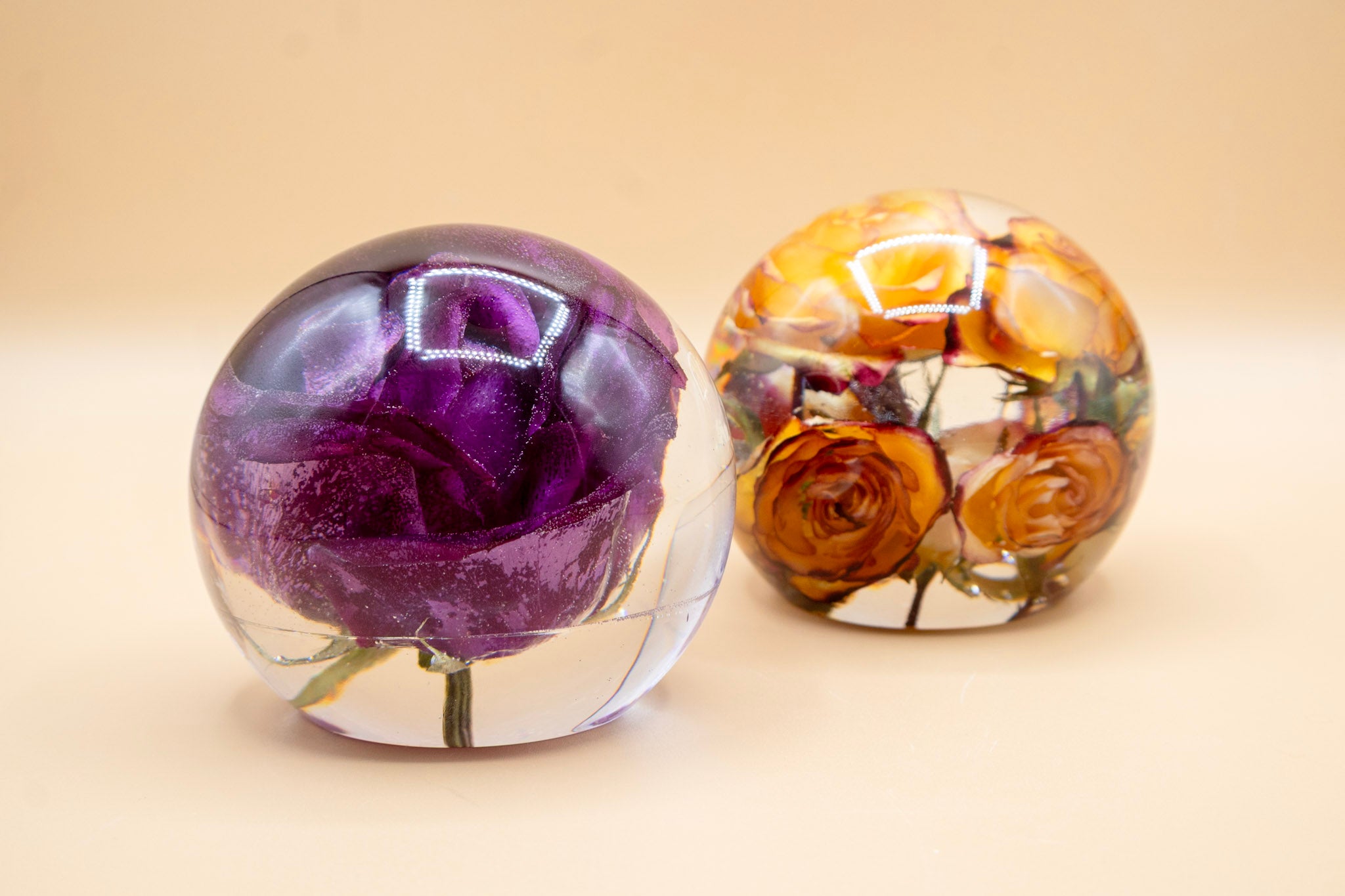 Two 5-inch resin sphere keepsakes preserving a purple rose and clustered orange roses, flower preservation display balls.