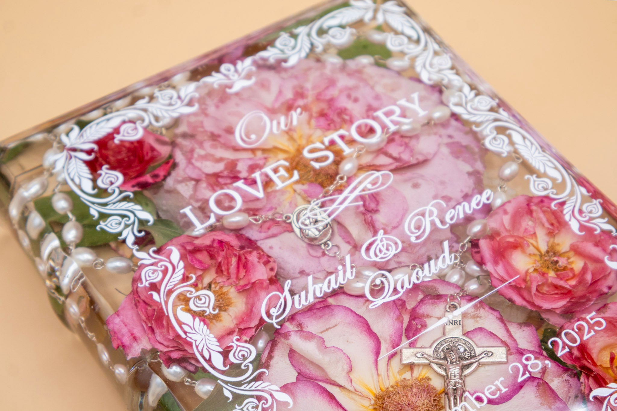 Book-shaped resin keepsake preserving pink wedding roses and a pearl rosary, personalized with a couple's names and date.