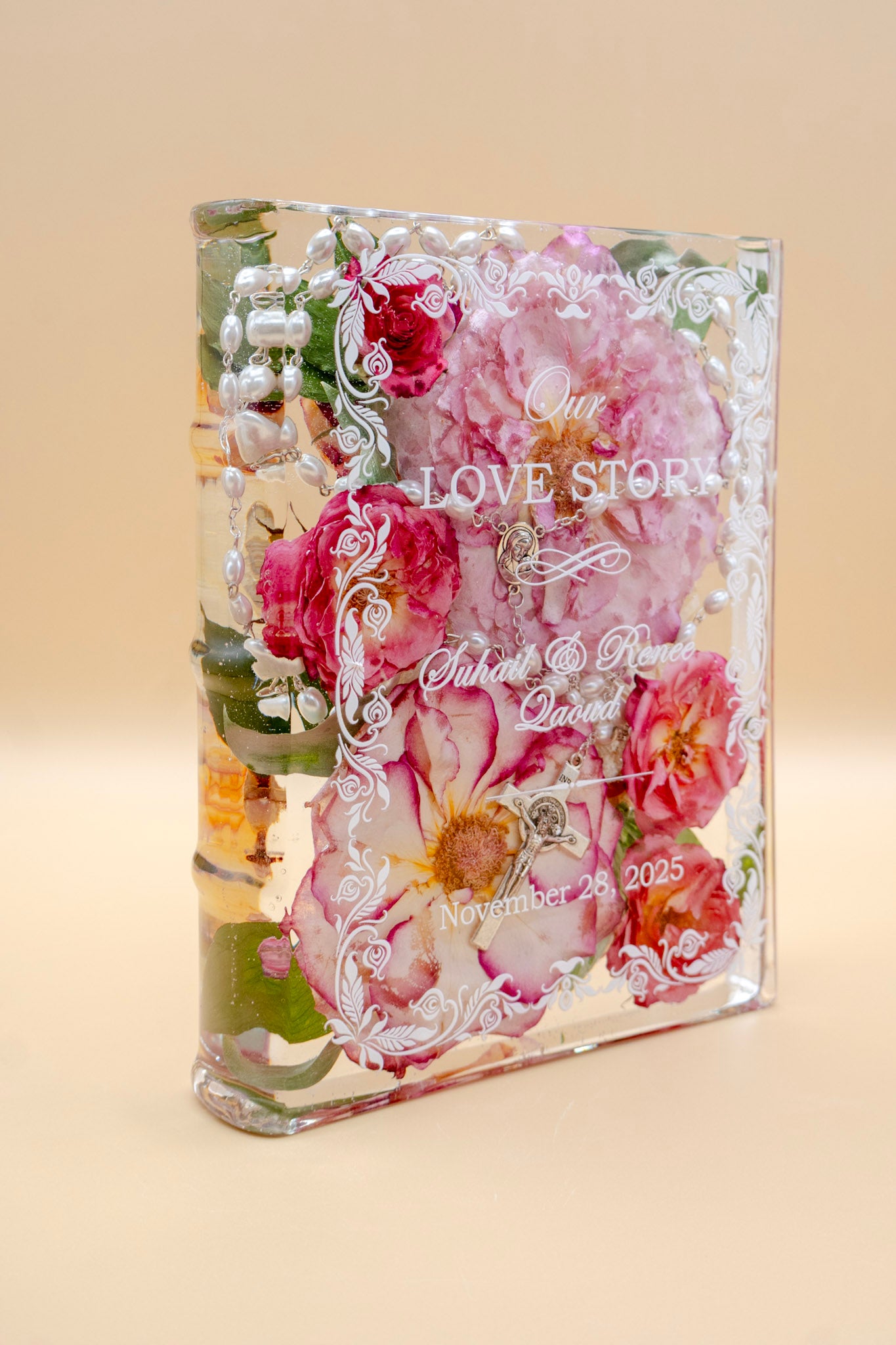 Book-shaped resin keepsake preserving pink wedding roses and a pearl rosary, personalized with a couple's names and date.