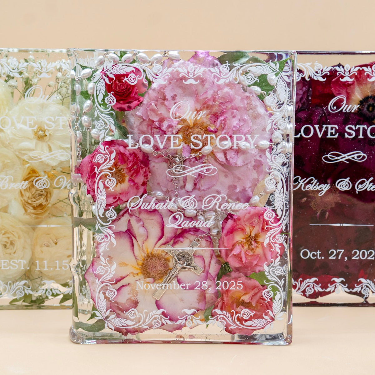 Three book-shaped resin keepsakes preserving white, pink, and burgundy wedding roses with names and dates, one with a rosary.