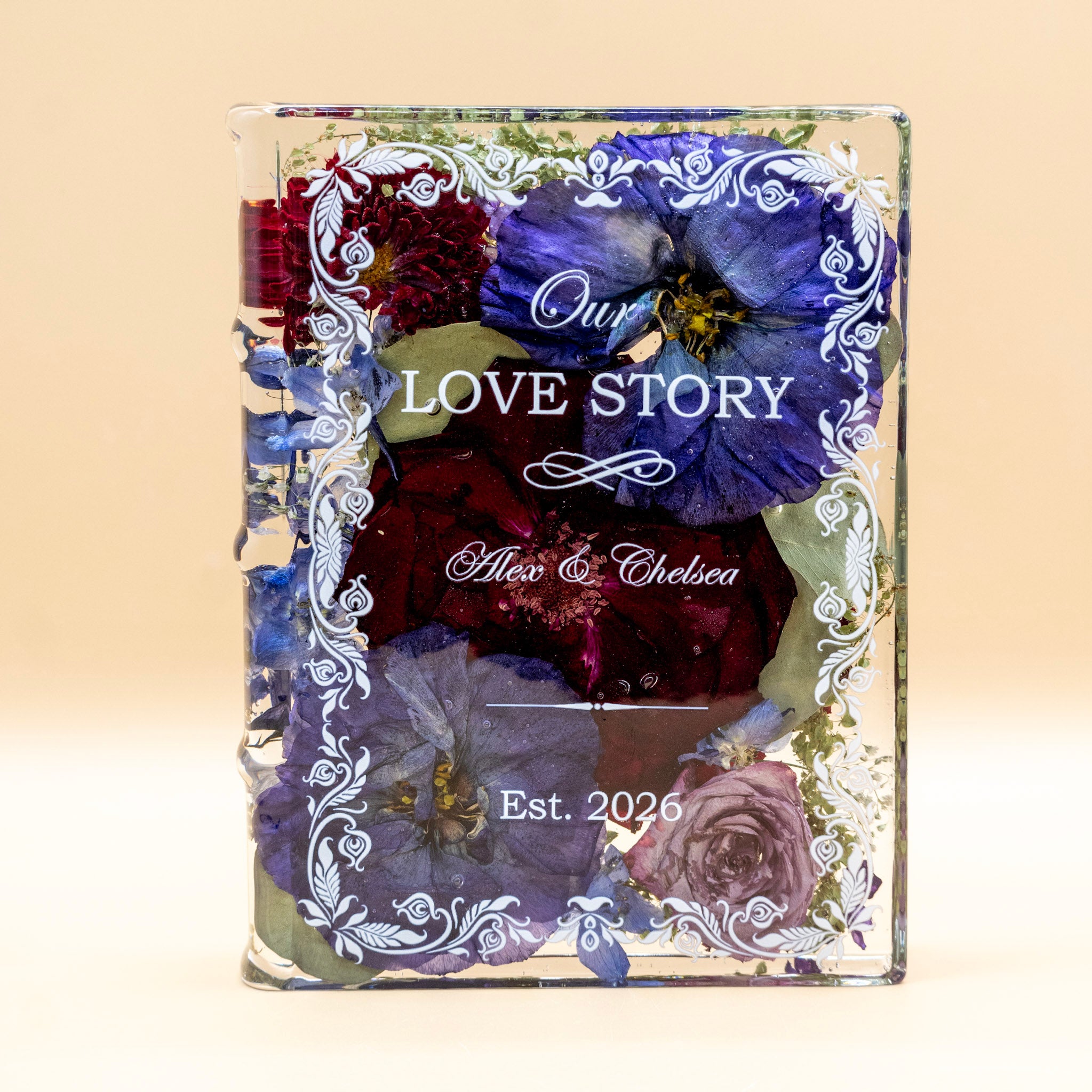 Book-shaped resin keepsake with preserved purple pansies, red mums, roses and delphinium, personalized with a couple's names and wedding date.