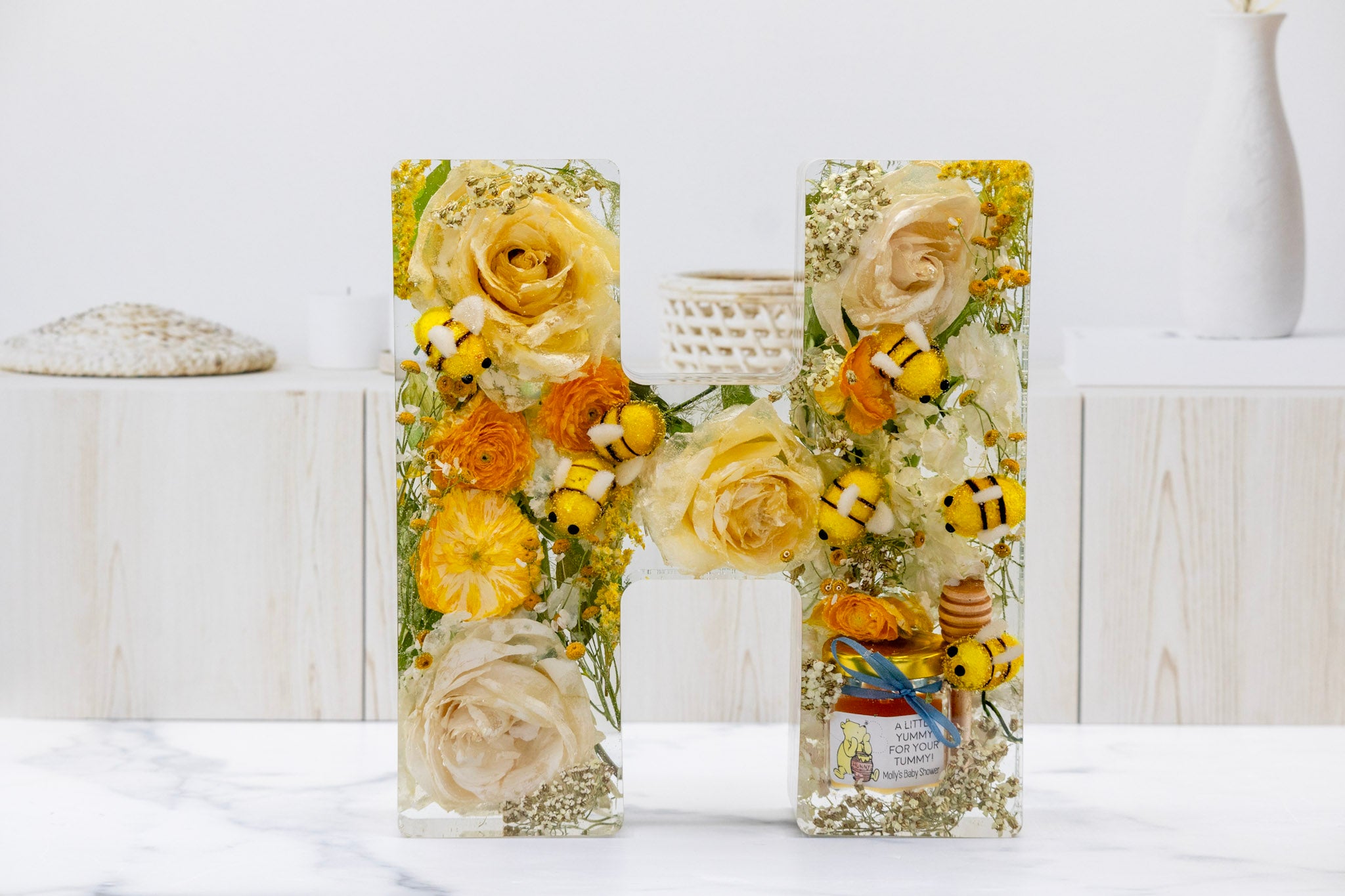 baby shower flower preservation letter 'H' made of preserved flowers, baby bees and honey jar favor on a white background